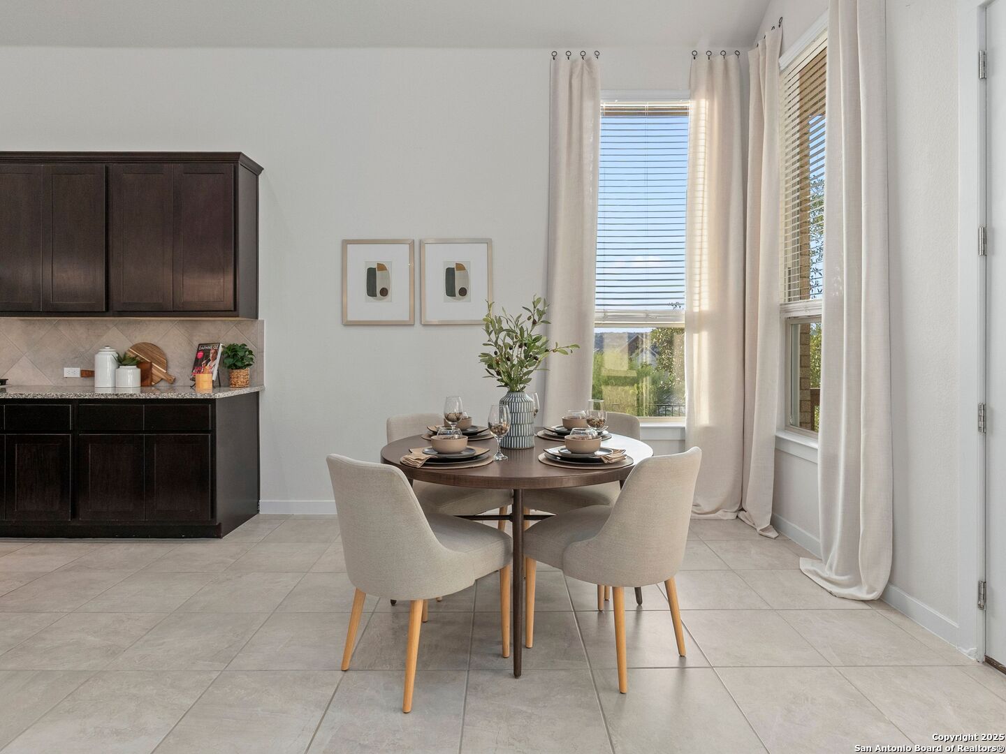 Dining area with a round set table, upholstered chairs, and tall curtained windows.