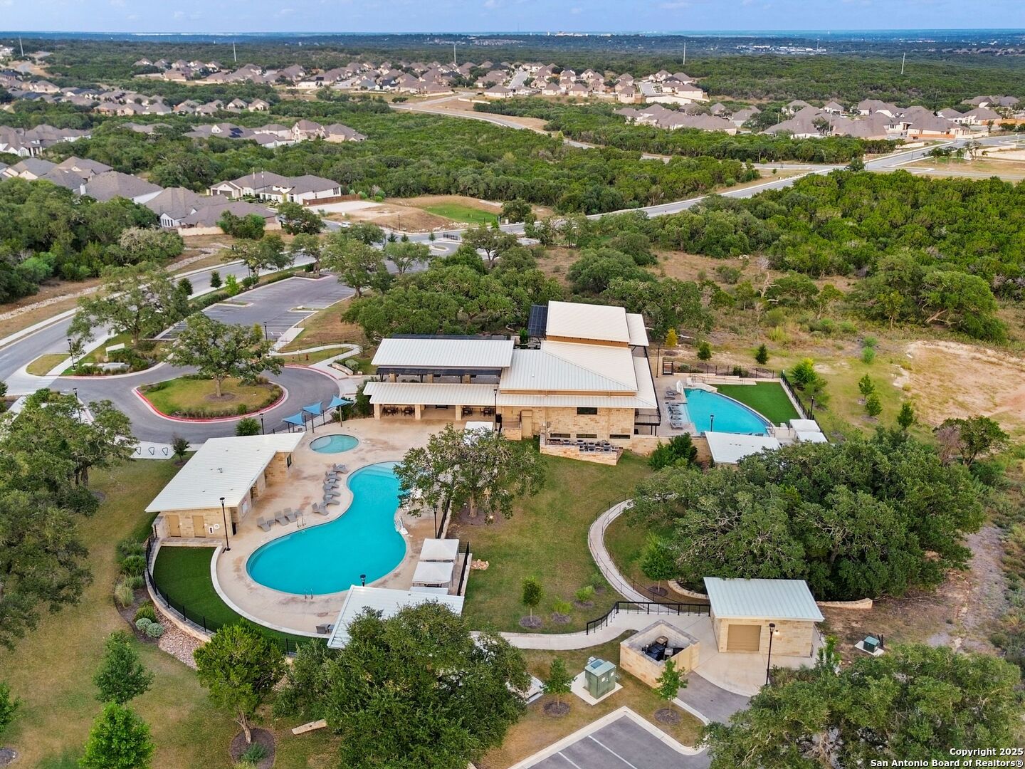 Aerial view of a neighborhood clubhouse and swimming pools surrounded by trees and homes.