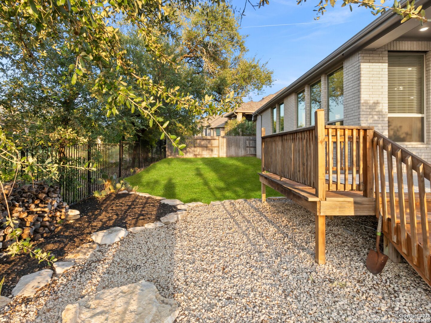 Brick home’s backyard with a raised wooden deck, gravel landscaping, lawn, and mature trees.