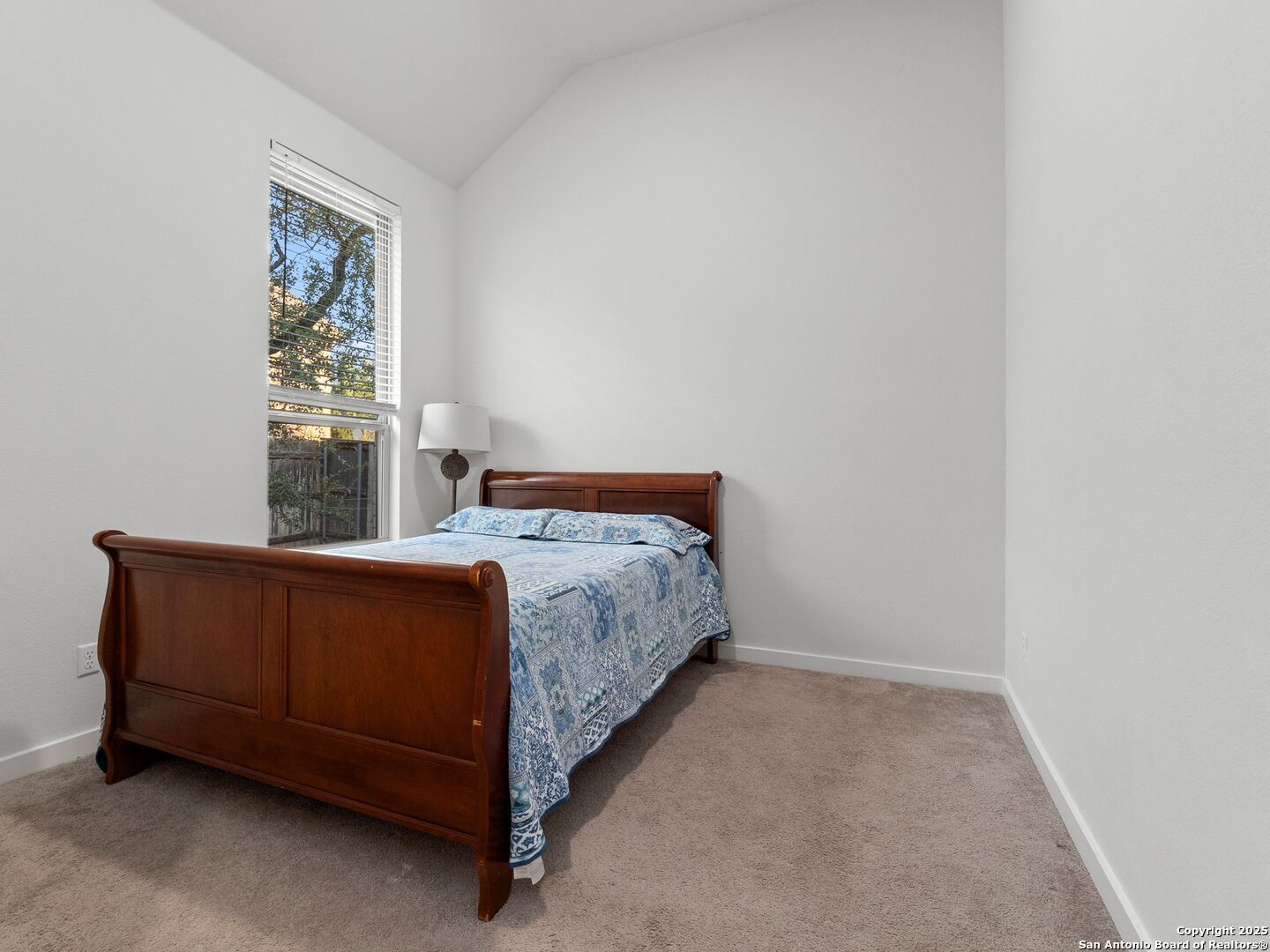 Furnished bedroom with a dark wood bed and blue patterned bedding beside a tall window.