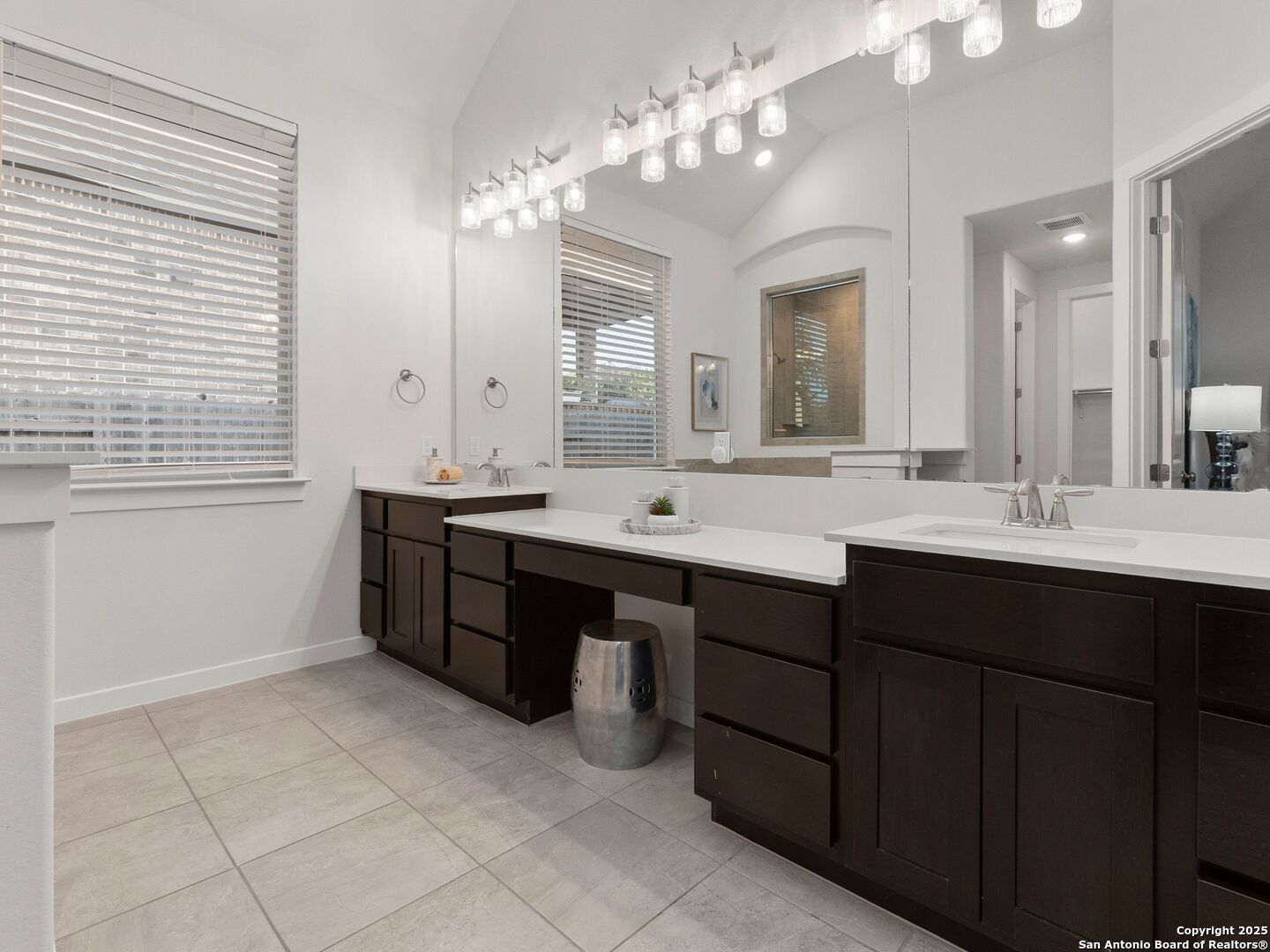 Bathroom with a dark double vanity, mirrored wall, and rows of glass pendant lights.