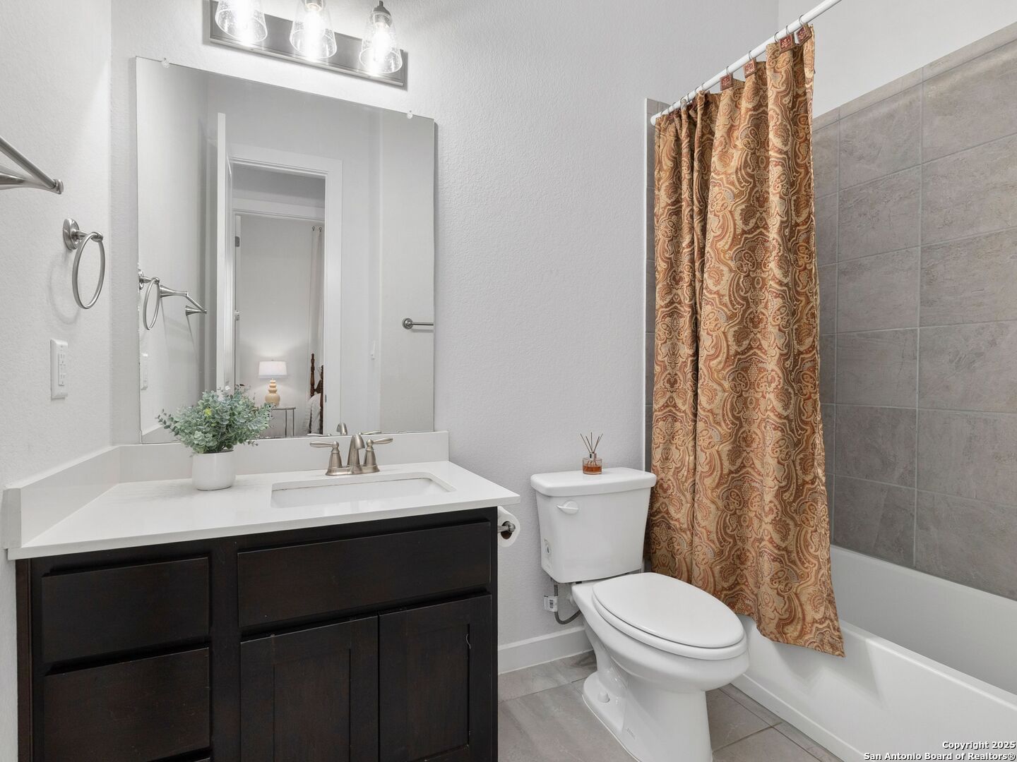 Bathroom with a dark wood vanity and patterned shower curtain beside a gray-tiled tub.