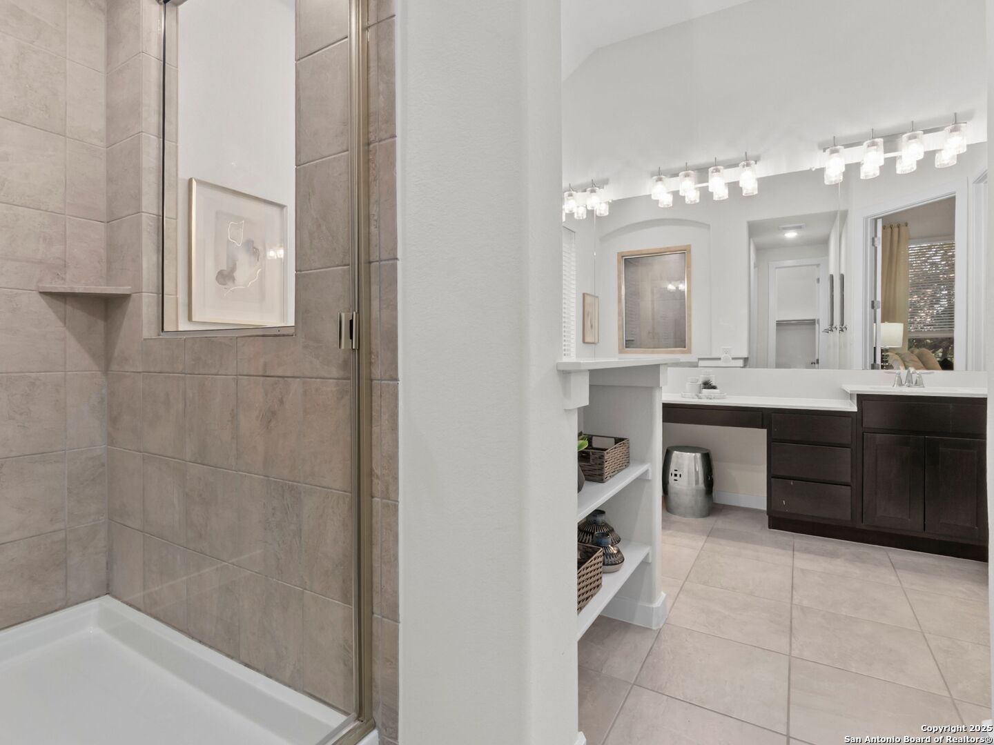 Bathroom with a tiled glass shower, dark wood vanity, large mirrors, and bright vanity lights.