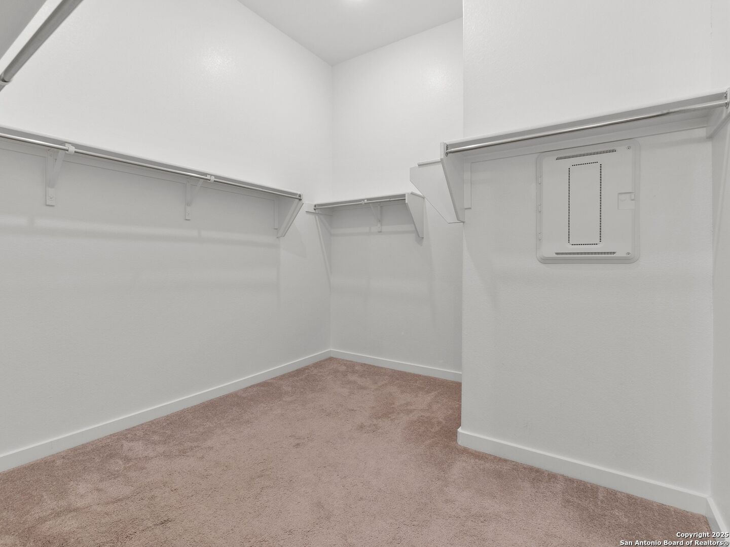 Empty walk-in closet with beige carpet and built-in shelves and hanging rods along three walls.
