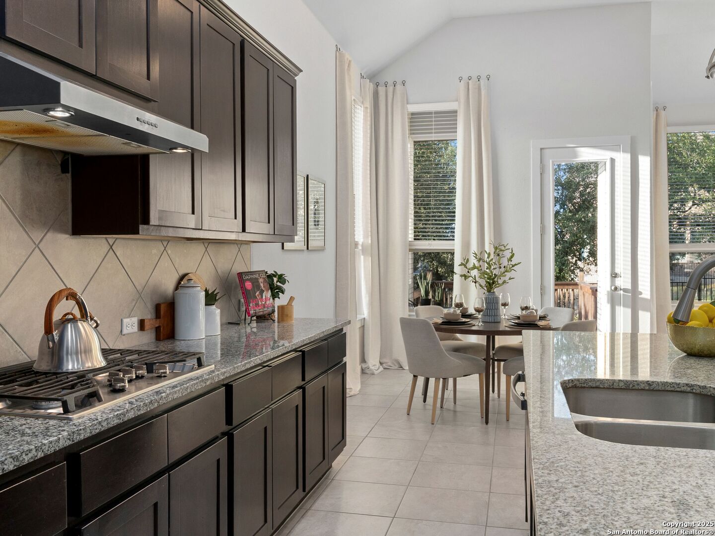 Kitchen with dark wood cabinets and granite counters, opening to a dining area beside a glass door.