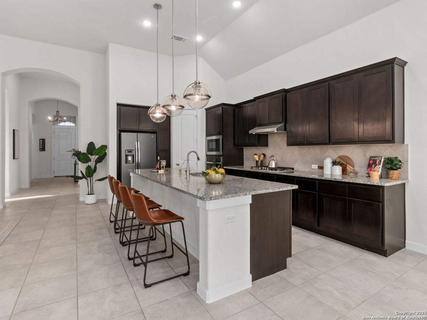 Kitchen with dark cabinets, stainless steel appliances, granite island, and three glass pendant lights.