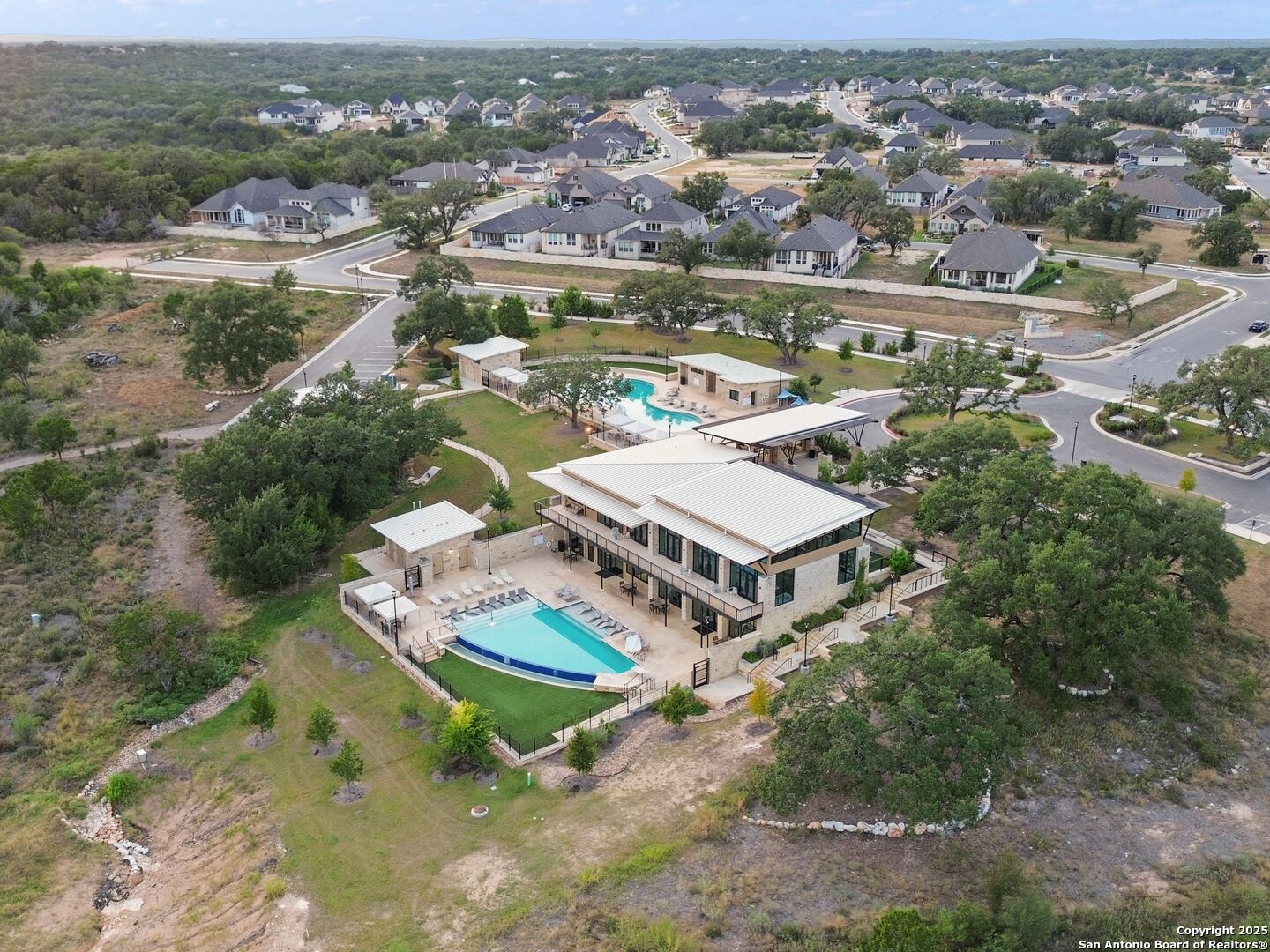 Aerial view of a residential community with a clubhouse, two swimming pools, and surrounding homes.