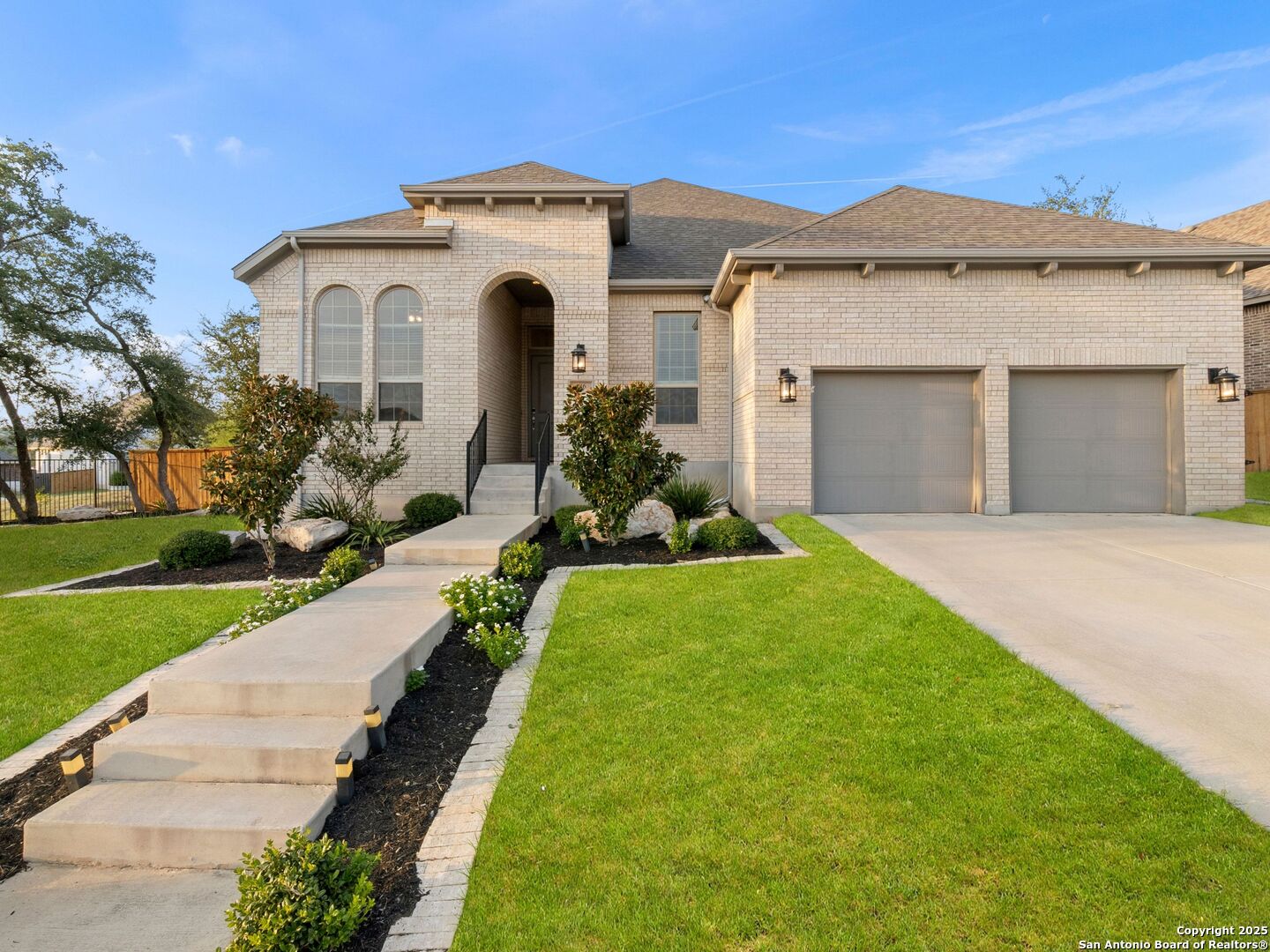 Brick home with arched entry, two-car garage, landscaped beds, and a front lawn.