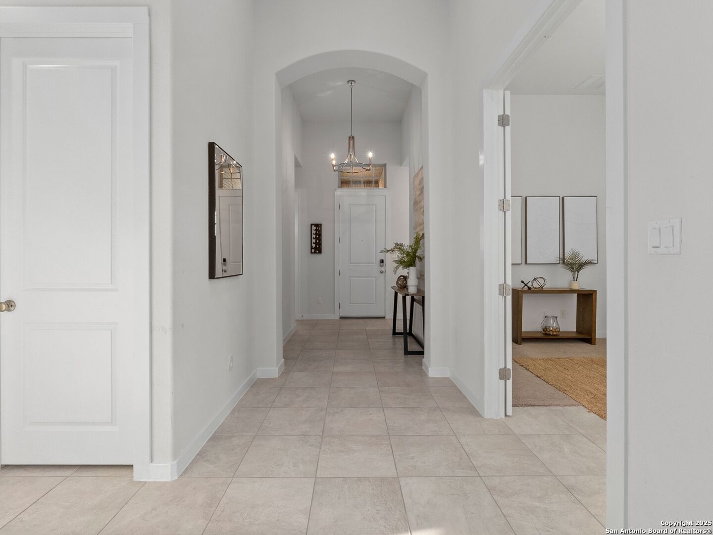Staged entry hall with tiled floors, an arched opening, chandelier, and console tables.