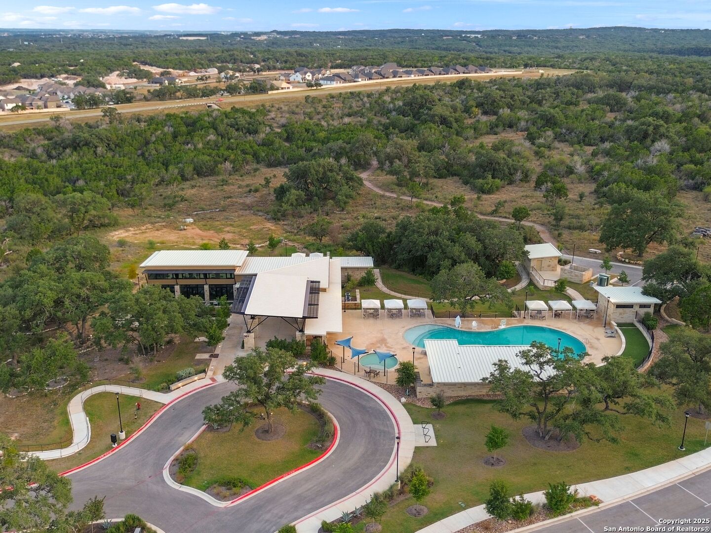 Aerial view of a community pool and clubhouse surrounded by trees.