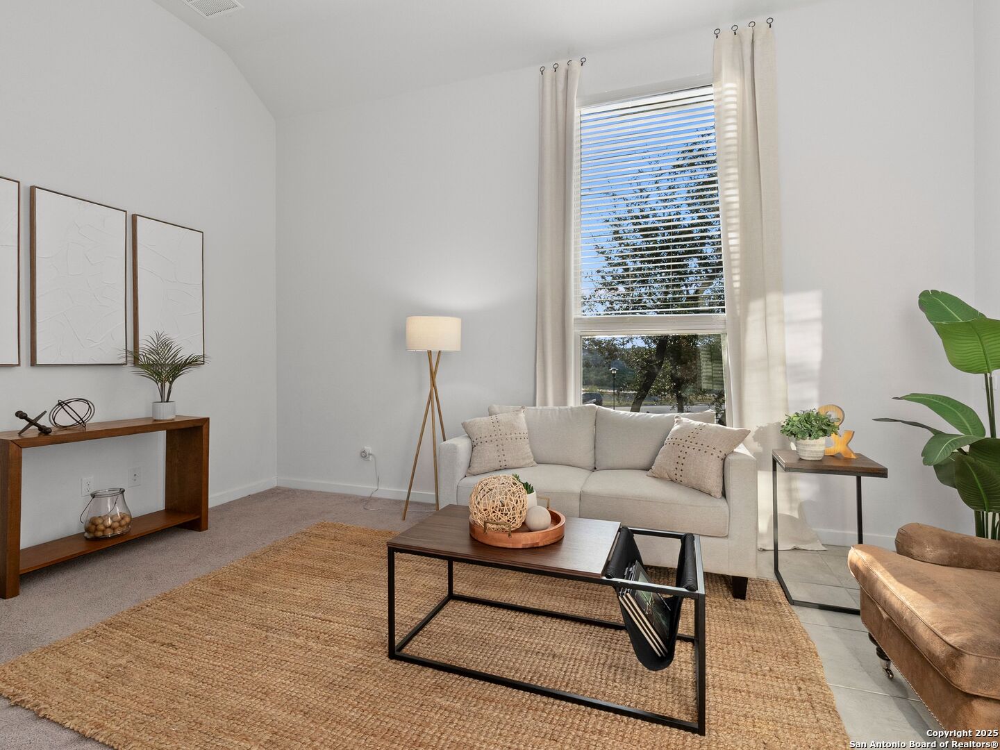 Staged living room with a tall curtained window, neutral sofa, and woven rug.