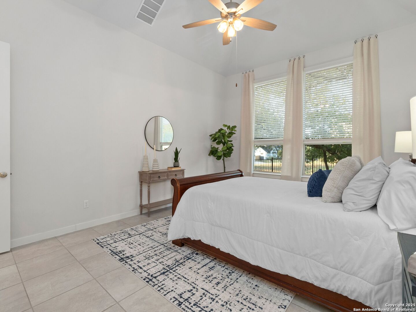 Staged bedroom with white bedding, a dark wood bed, tall curtained windows, and a ceiling fan.