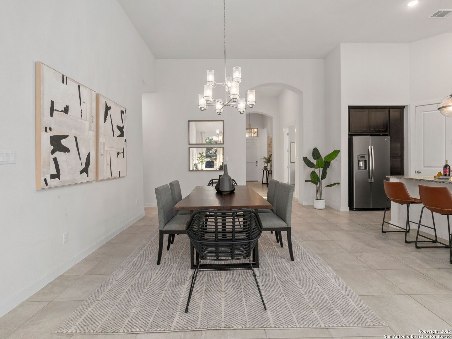 Dining room with a wood table, gray chairs, chandelier, and open kitchen.