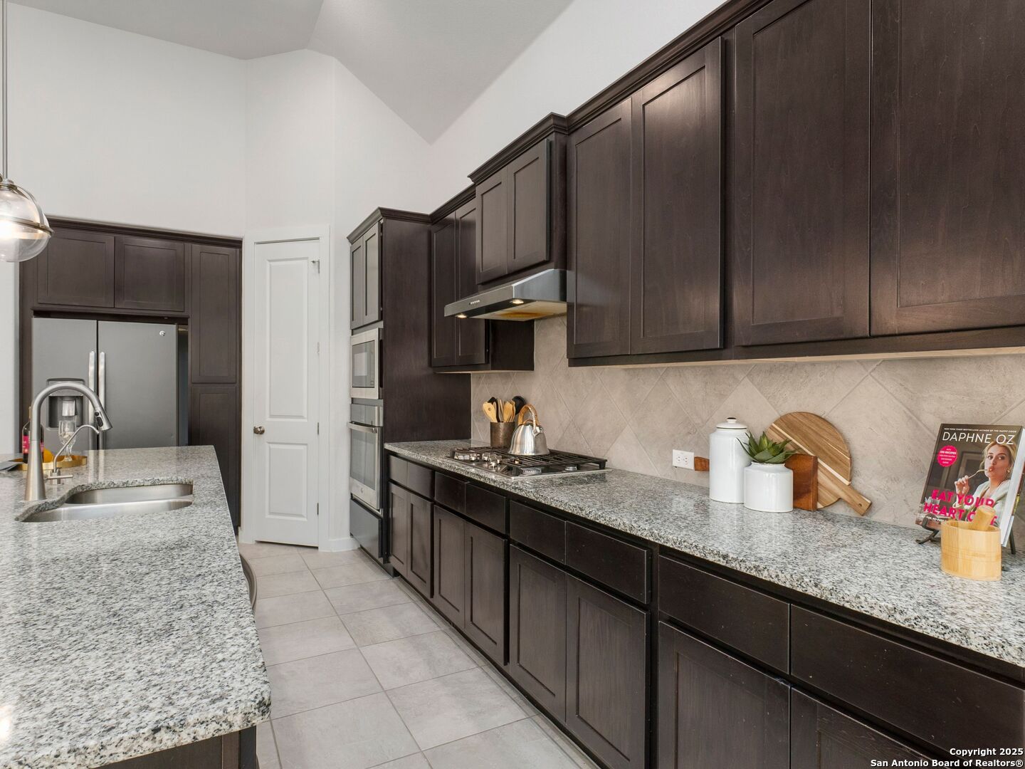 Kitchen with dark paneled cabinets, granite counters, a large sink island, and stainless steel appliances.