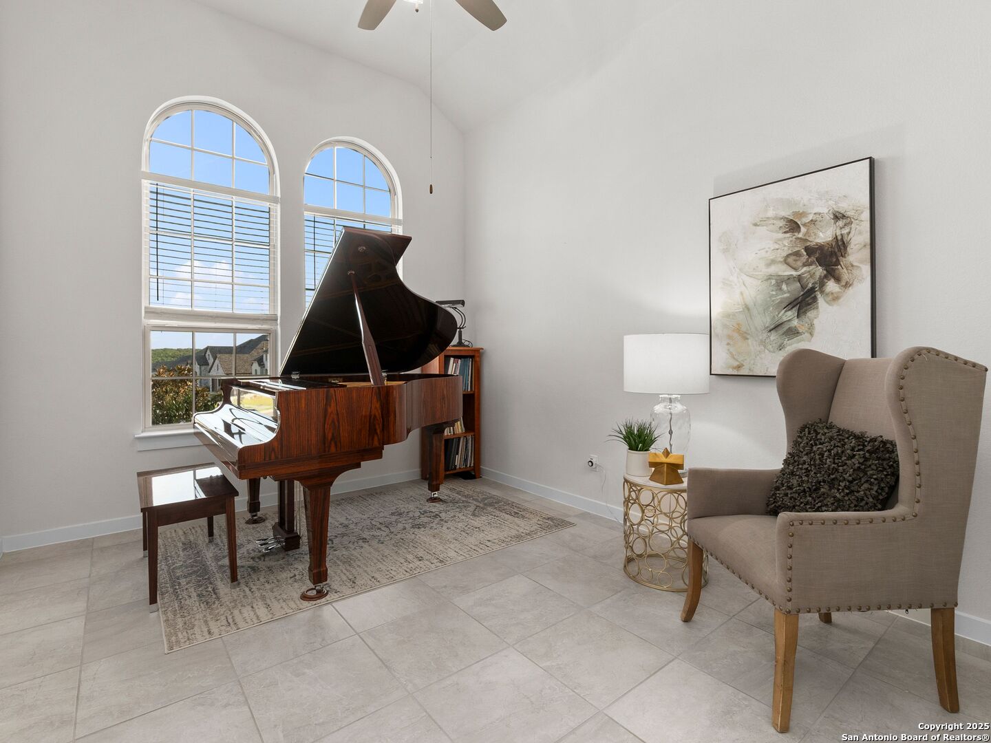Music room with a polished grand piano, arched windows, and a tufted wingback chair.