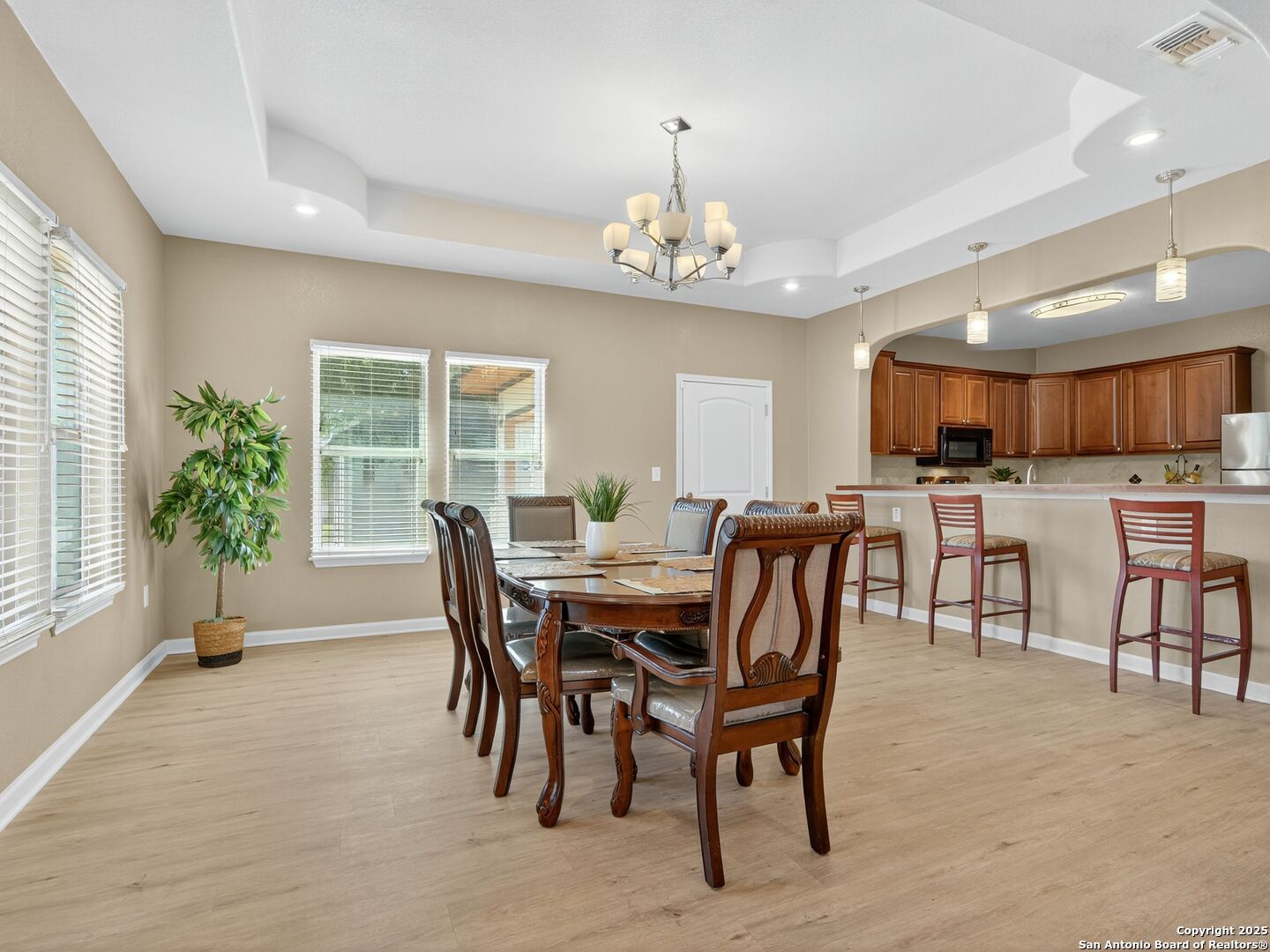 Dining area with a wooden table and chandelier beside an open kitchen with a breakfast bar.