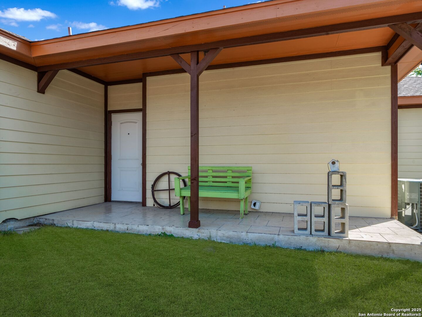 Covered rear patio with a bright green bench overlooking a neatly trimmed lawn.