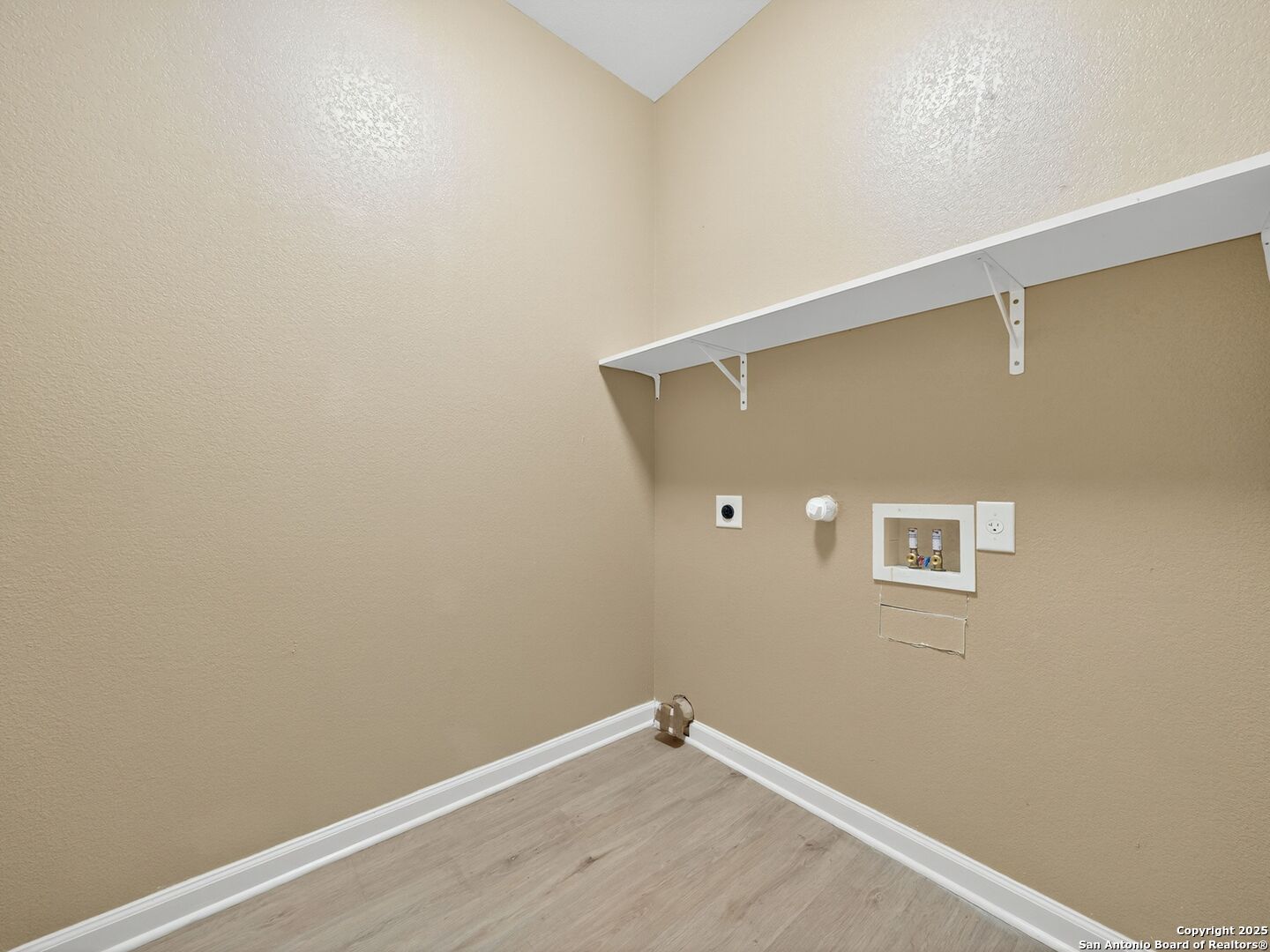 Empty laundry area with washer and dryer hookups, a wall shelf, and light wood-look flooring.
