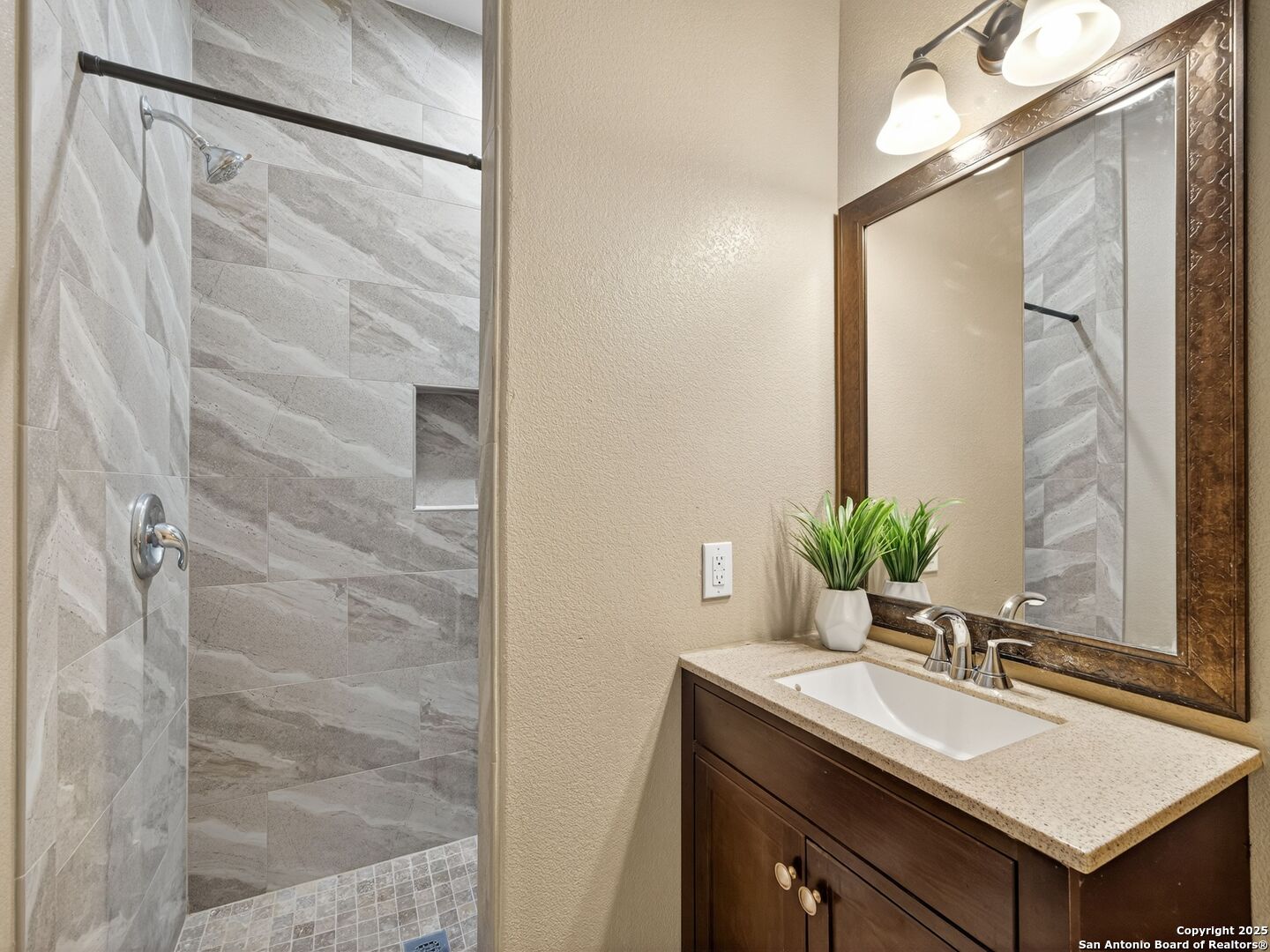 Bathroom with a gray tiled shower beside a dark wood vanity and large framed mirror.
