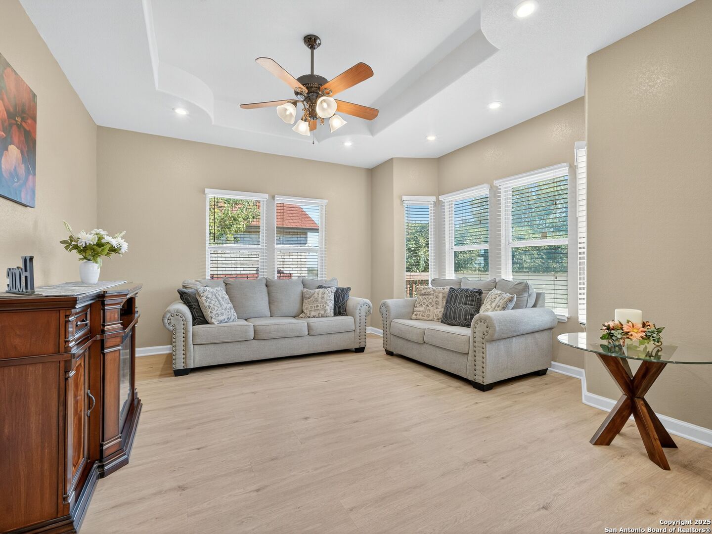 Living room with two gray sofas, a tray ceiling, ceiling fan, and bright windows.