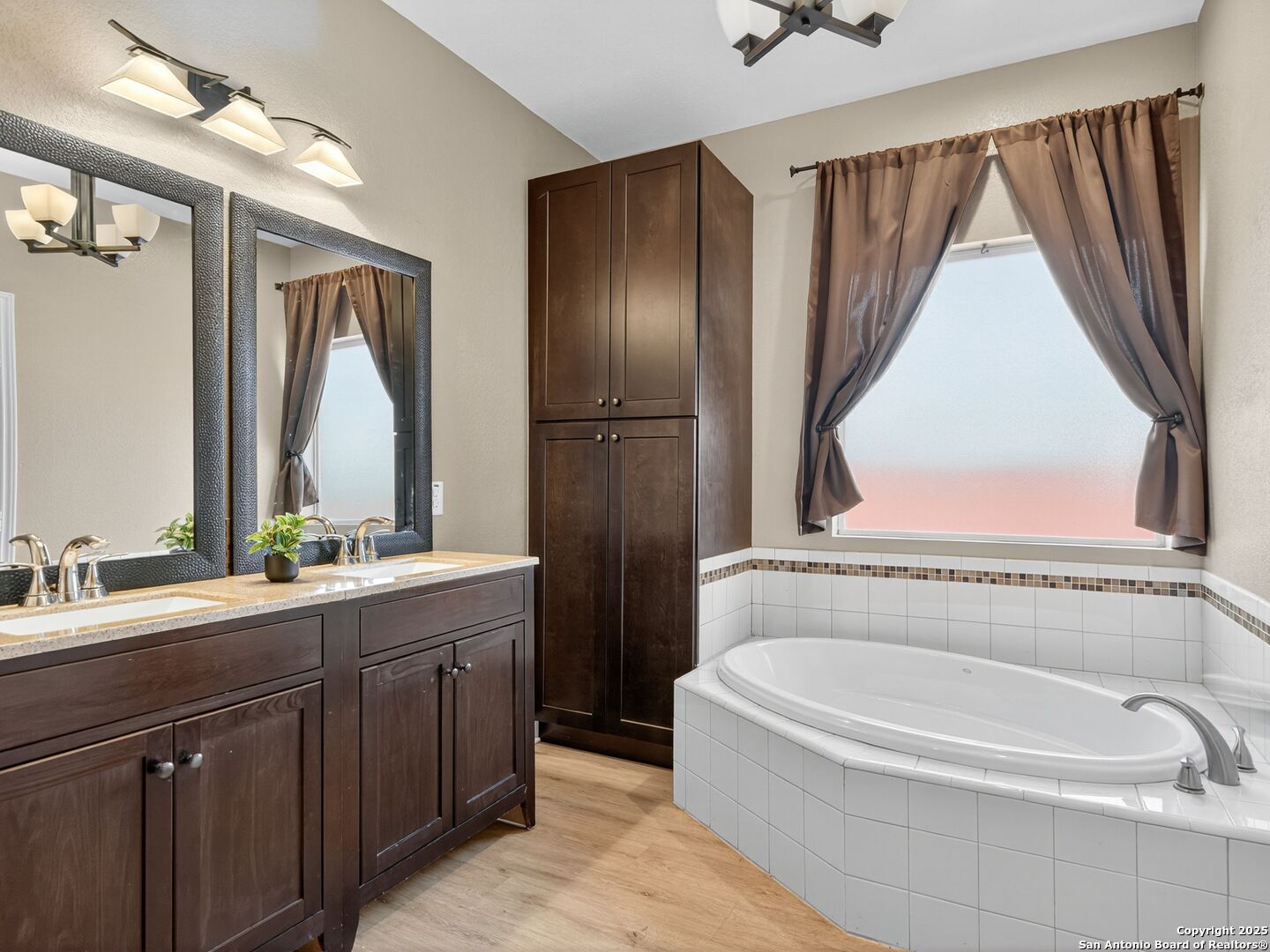 Bathroom with a dark wood double vanity, tall cabinets, and a white corner soaking tub.