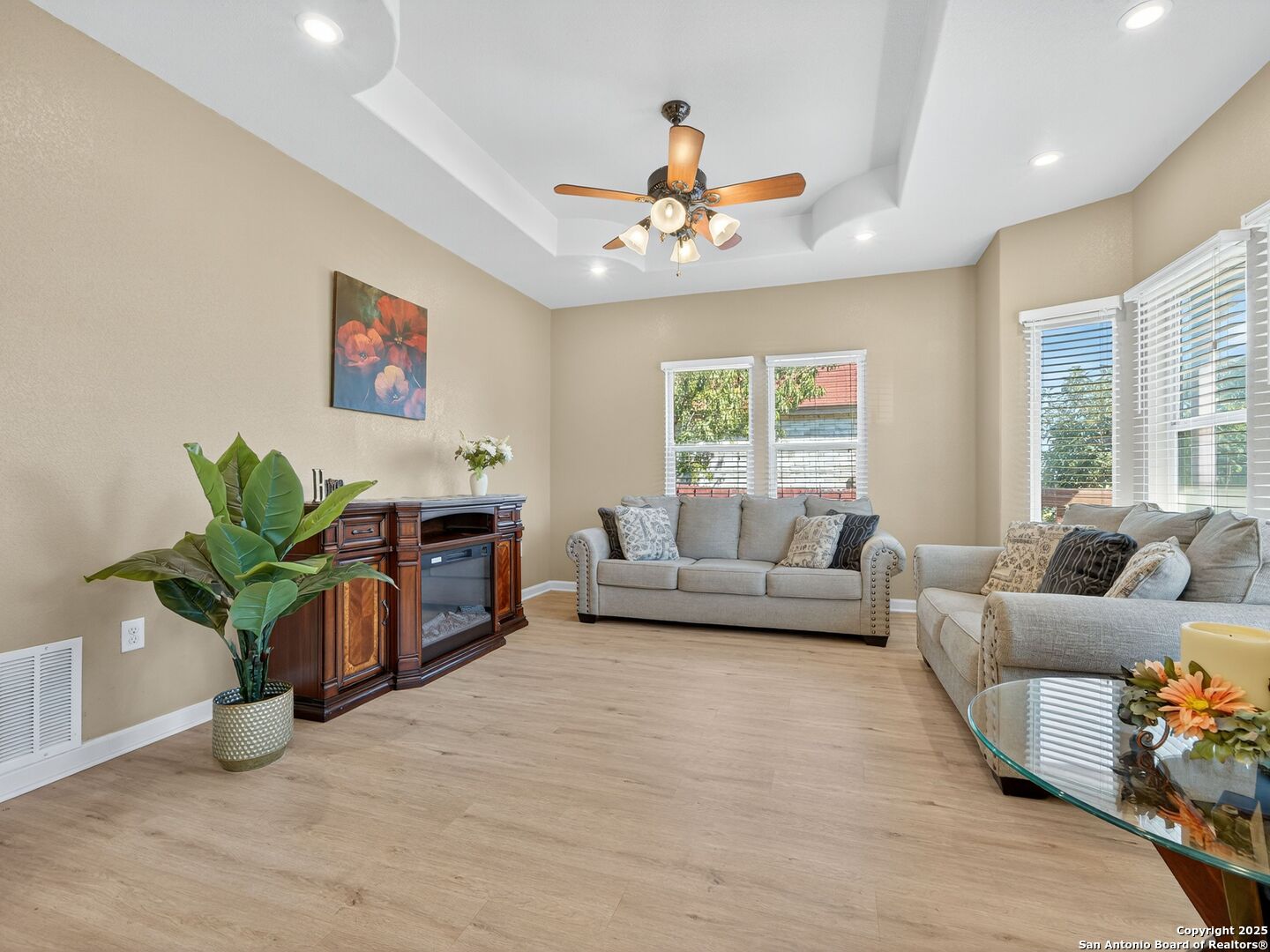 Living room with gray sofas, a tray ceiling, and large windows with white blinds.