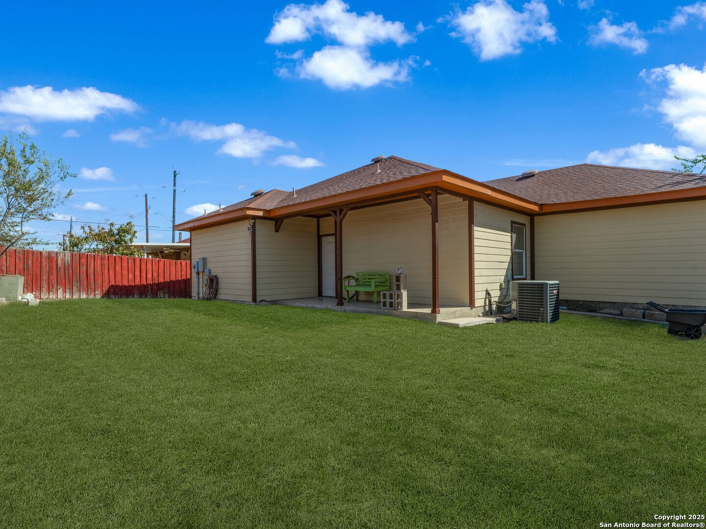 Home’s rear exterior with a covered patio, green bench, broad lawn, and red fence.