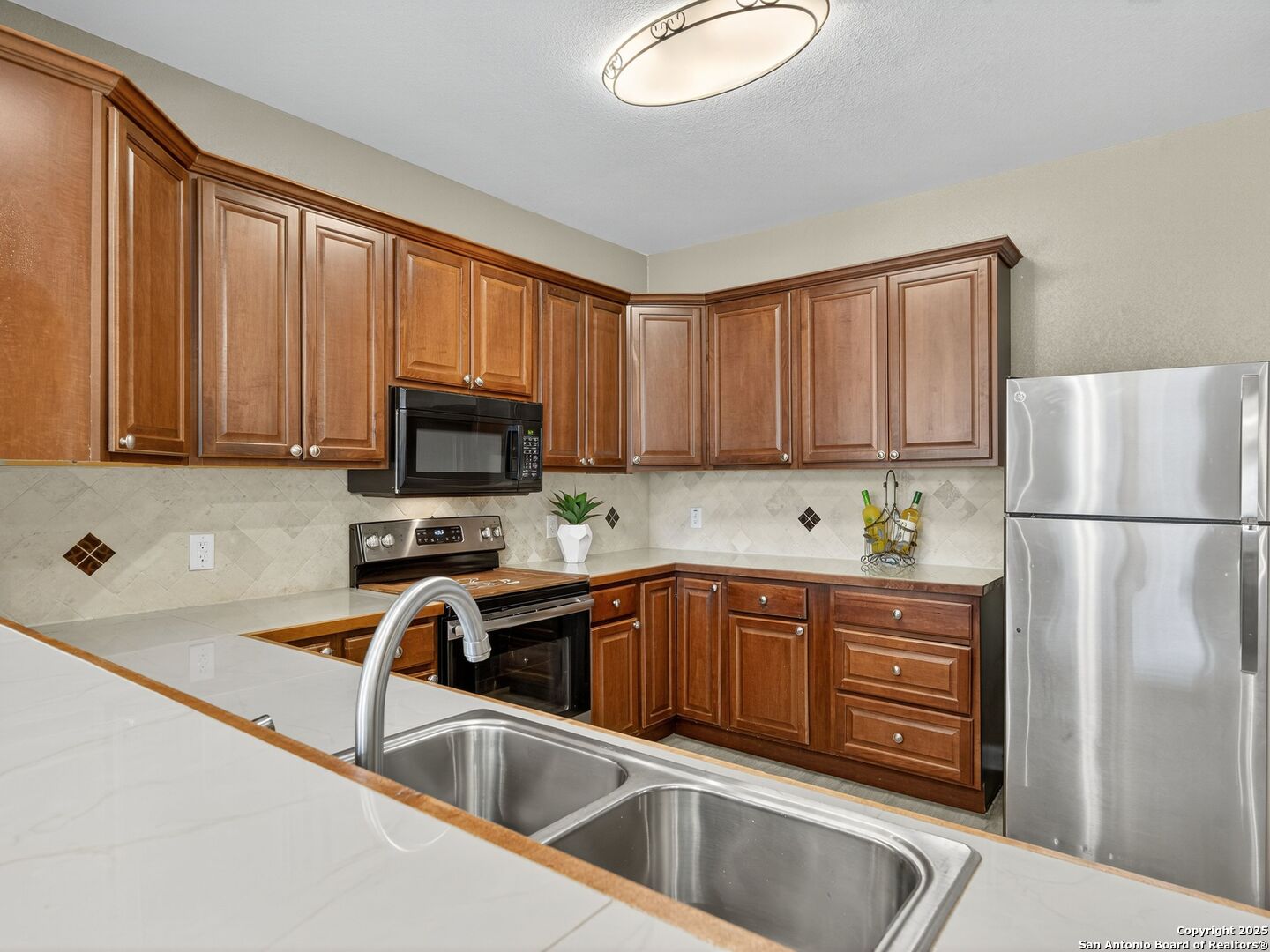 Kitchen with warm wood cabinets, stainless steel appliances, and a white peninsula with a double sink.