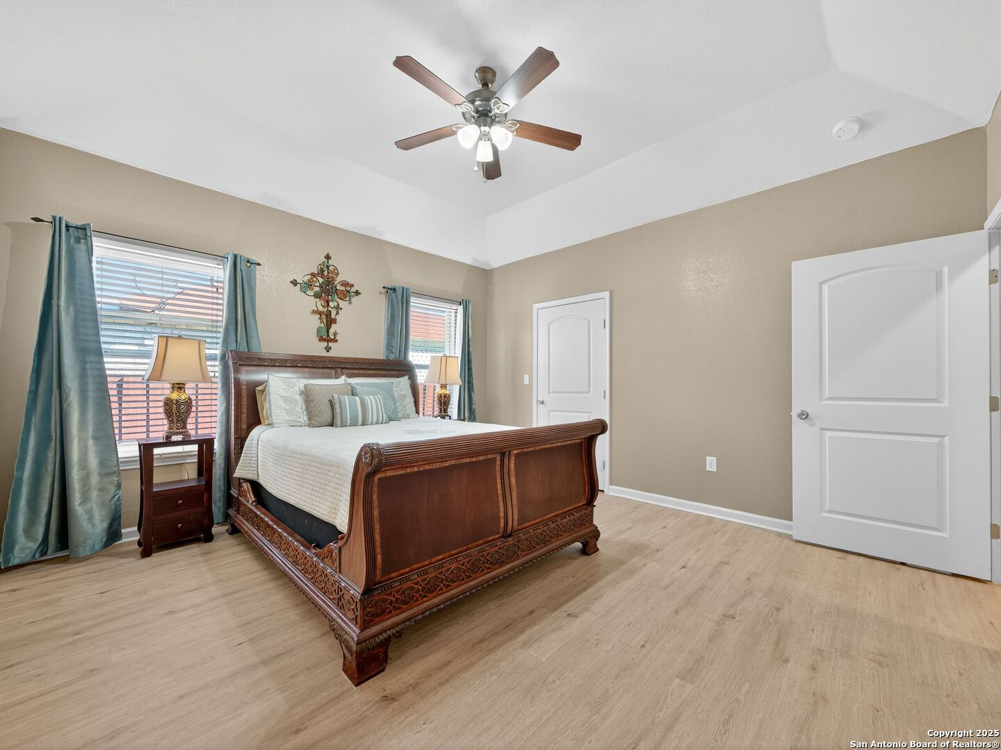 Furnished bedroom with a carved dark wood bed, teal curtains, and a ceiling fan.