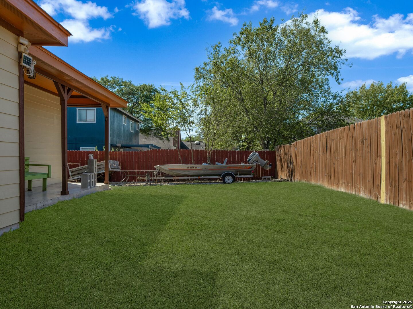 Backyard with a broad lawn, covered patio, wooden fences, and a boat on a trailer.