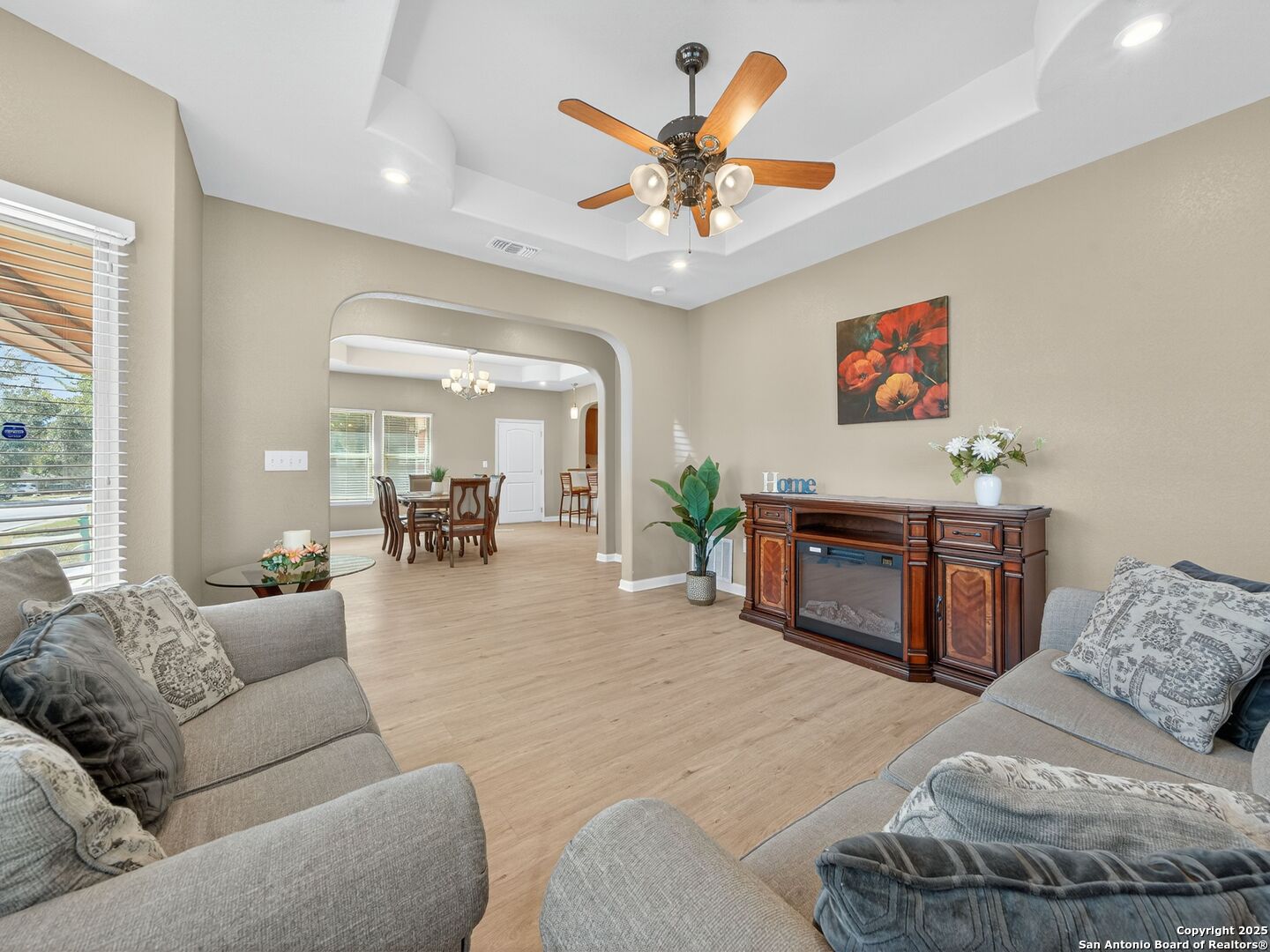 Furnished living room with a tray ceiling, gray sofas, and an arched opening to the dining area.