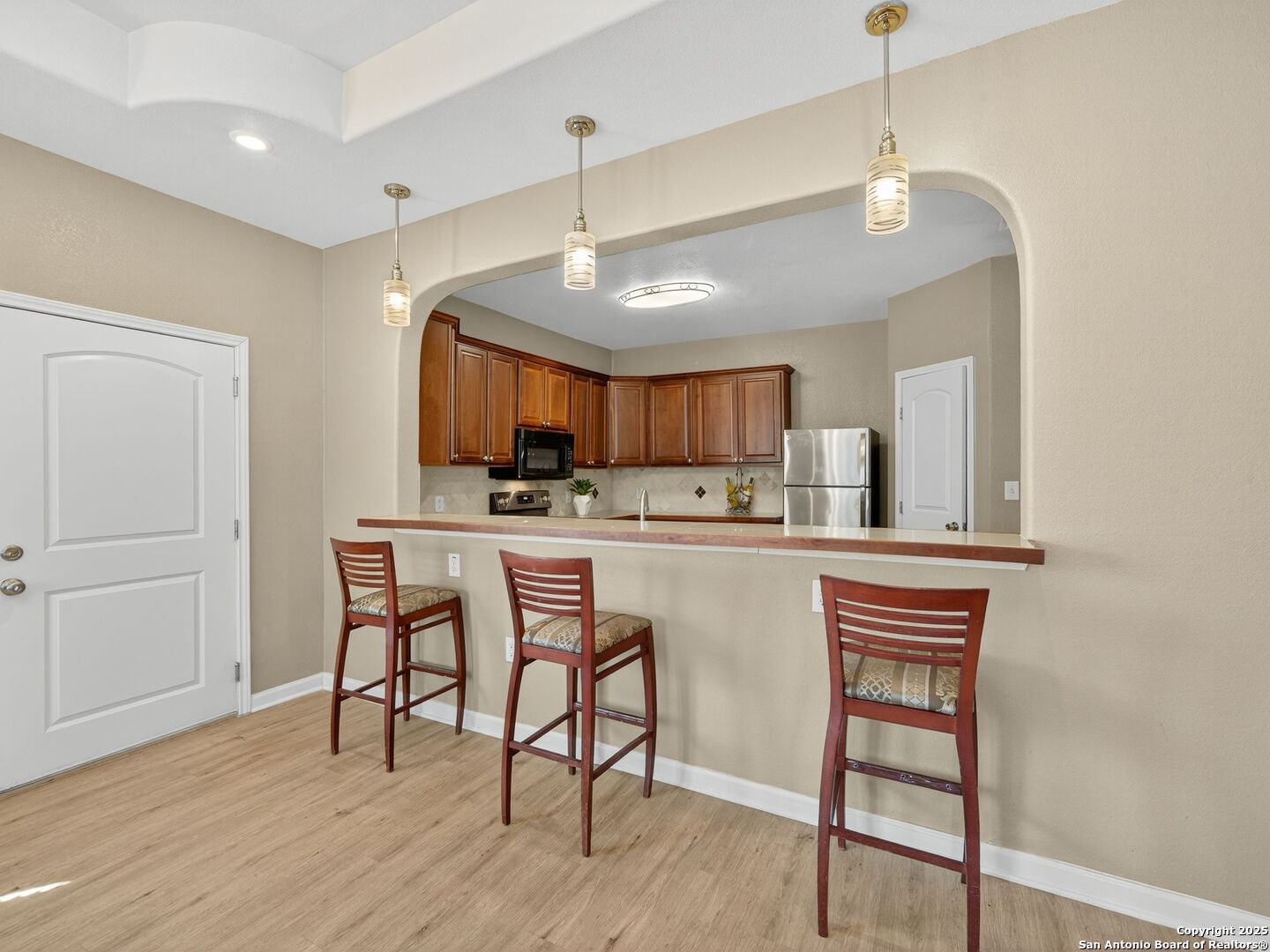 Kitchen with a long breakfast bar, three wooden stools, and warm wood cabinets.