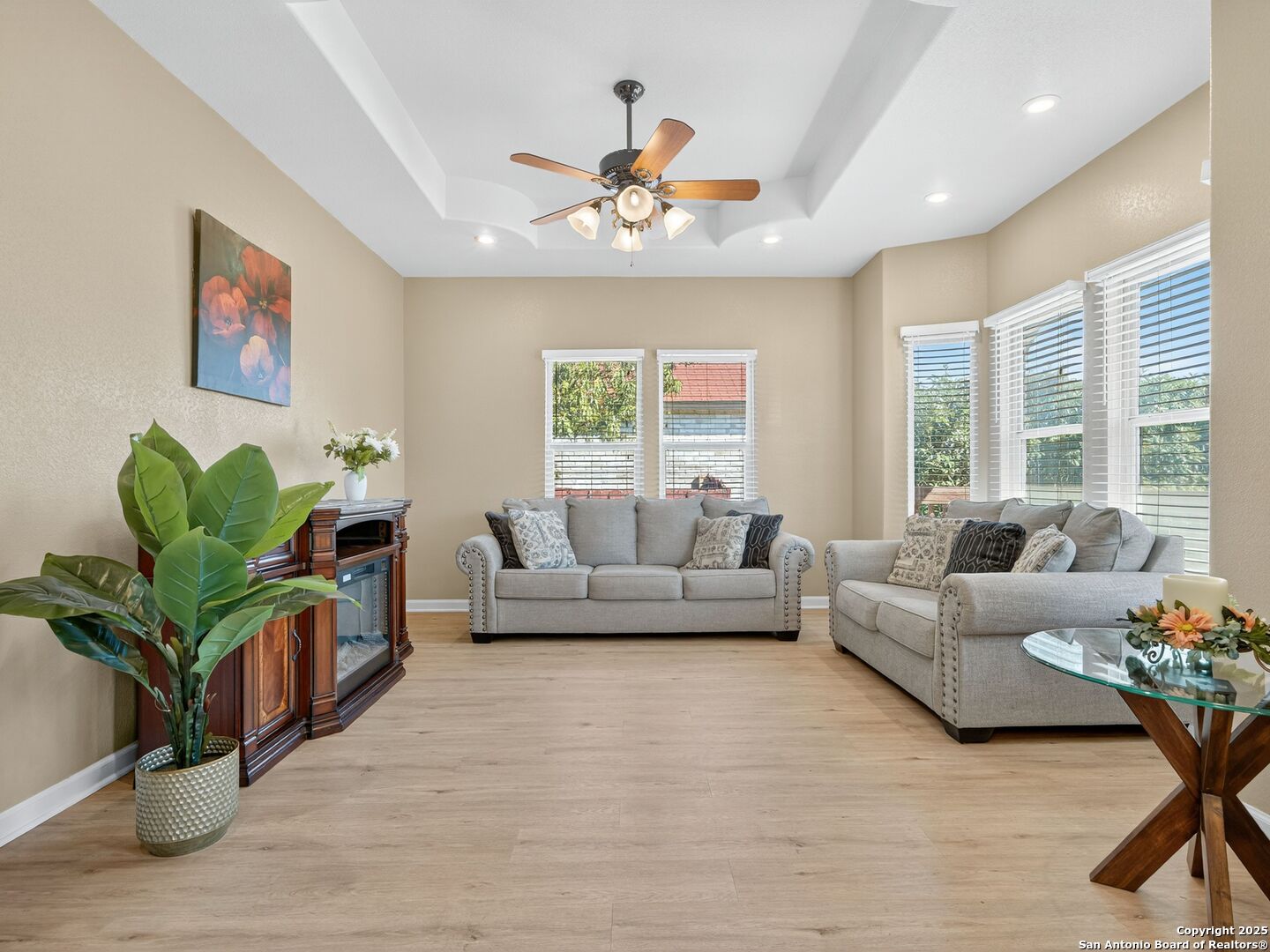 Living room with two gray sofas, a tray ceiling, and large windows with white blinds.