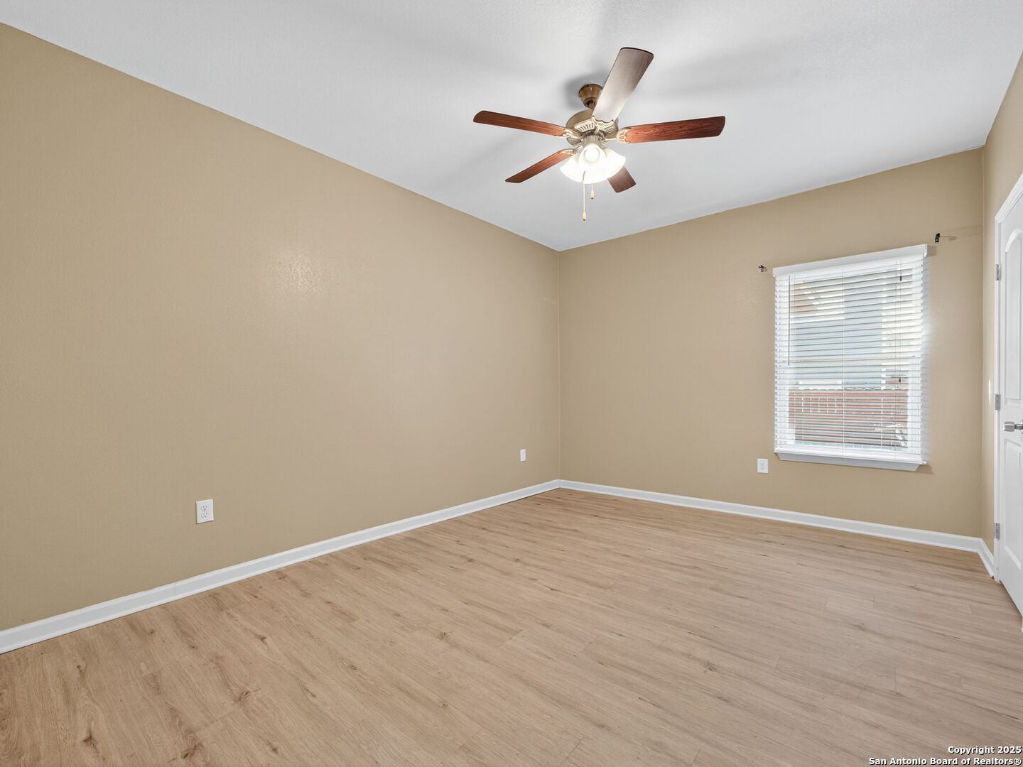 Vacant bedroom with light wood-look flooring, tan walls, and a ceiling fan.