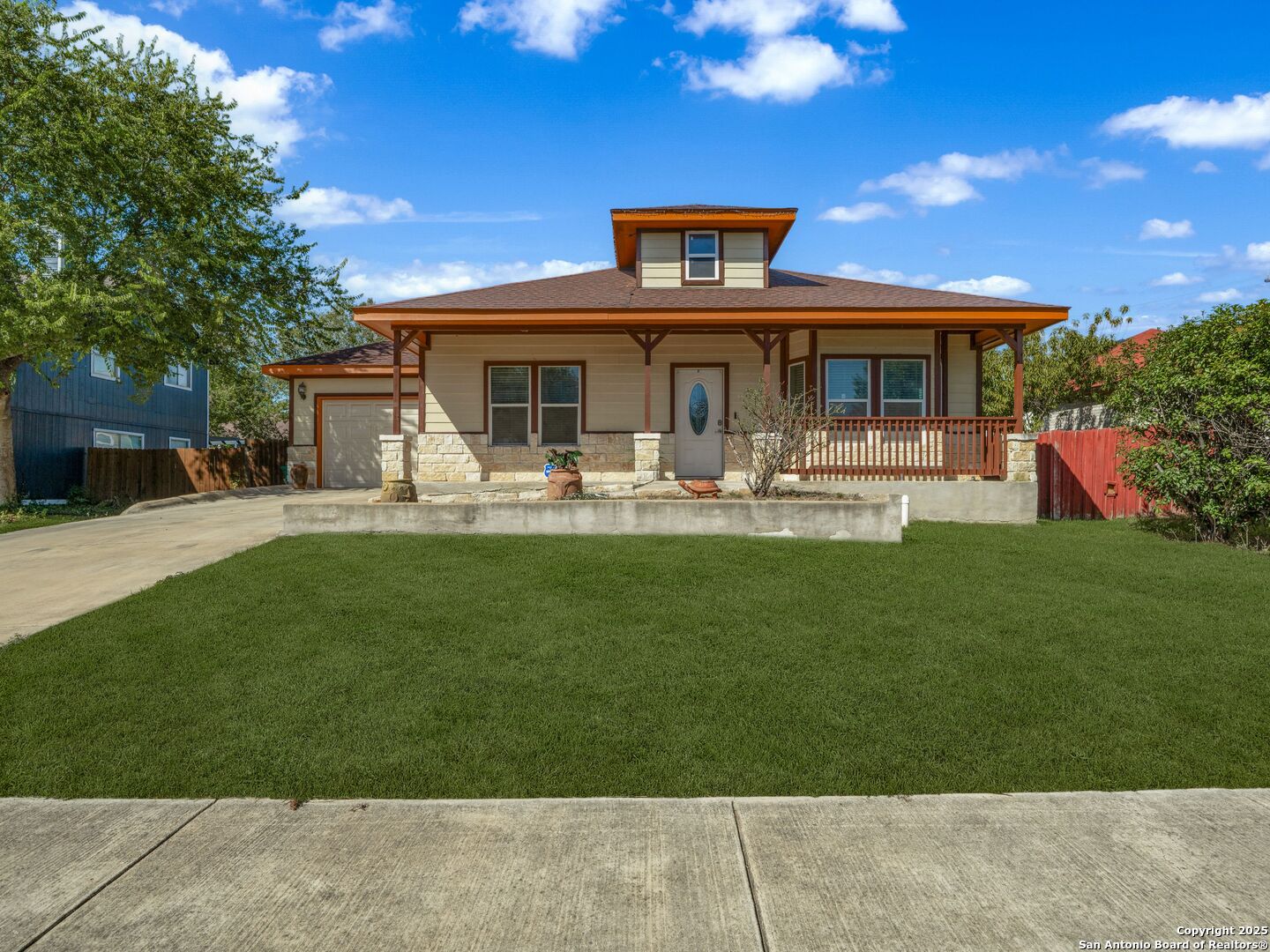 House with a covered front porch, stone facade, attached garage, and broad green lawn.