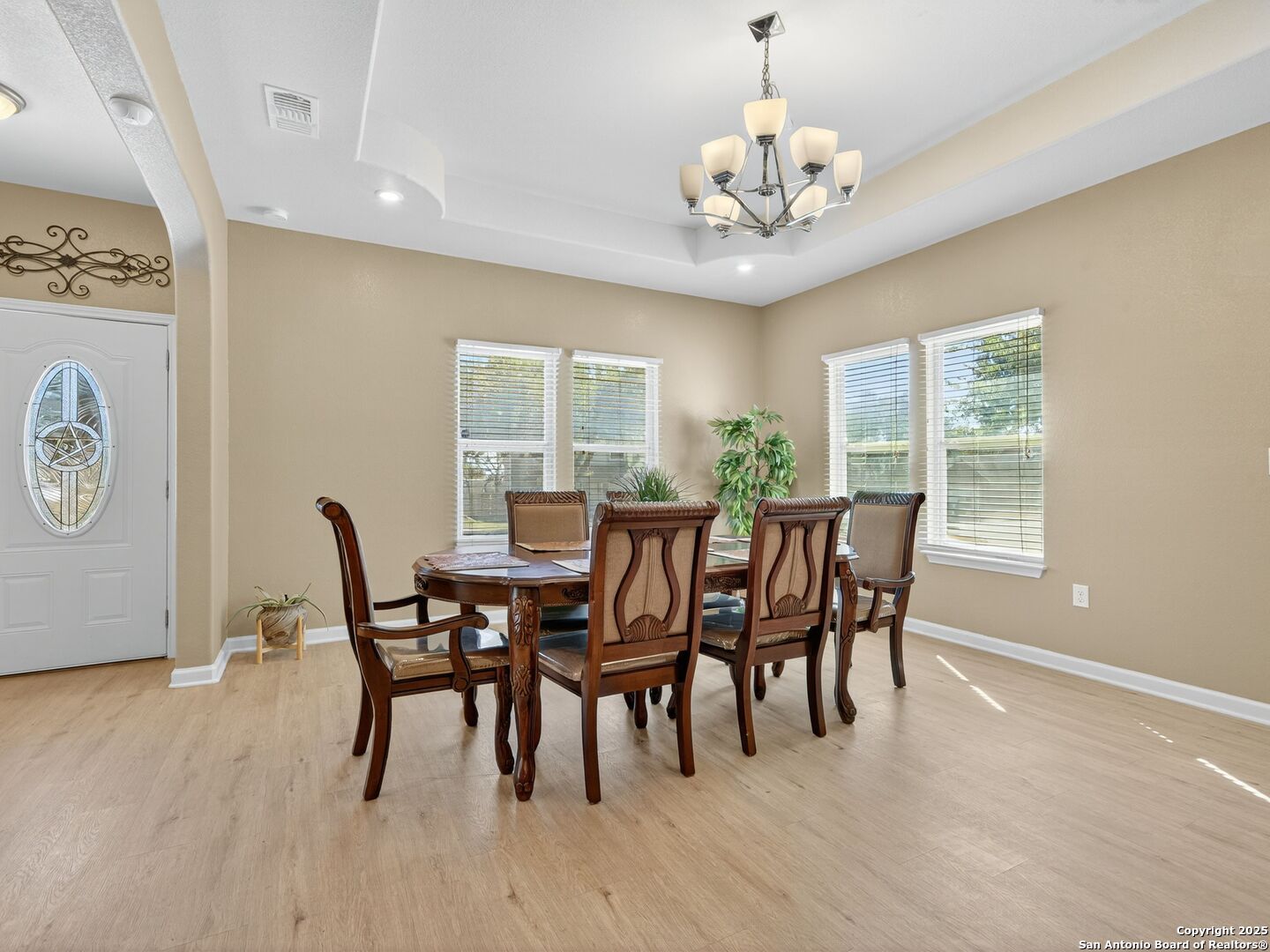 Dining room with a carved wood table, chandelier, tray ceiling, and multiple sunlit windows.