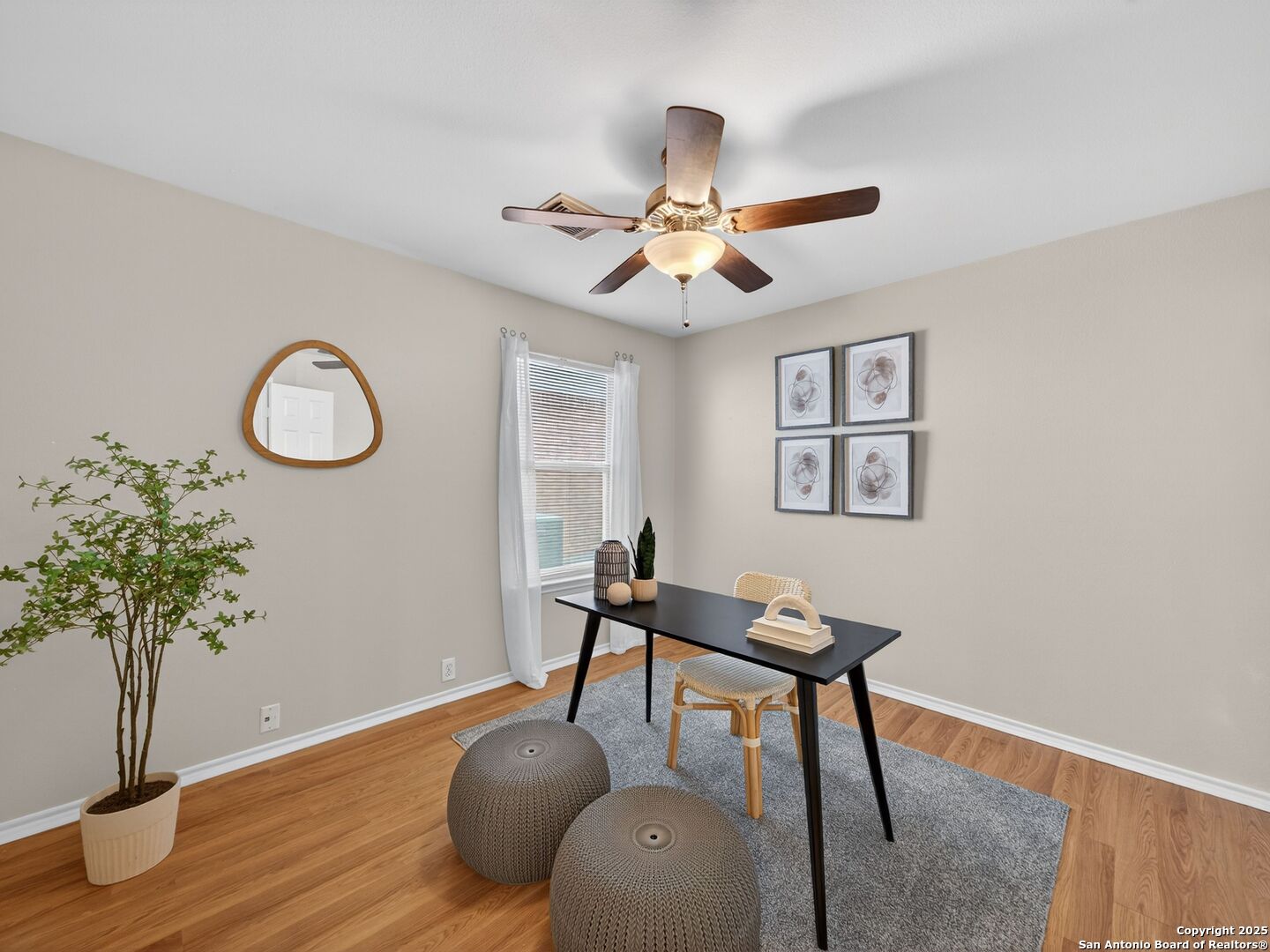 Staged home office with a black desk, woven chair, gray rug, and wood flooring.