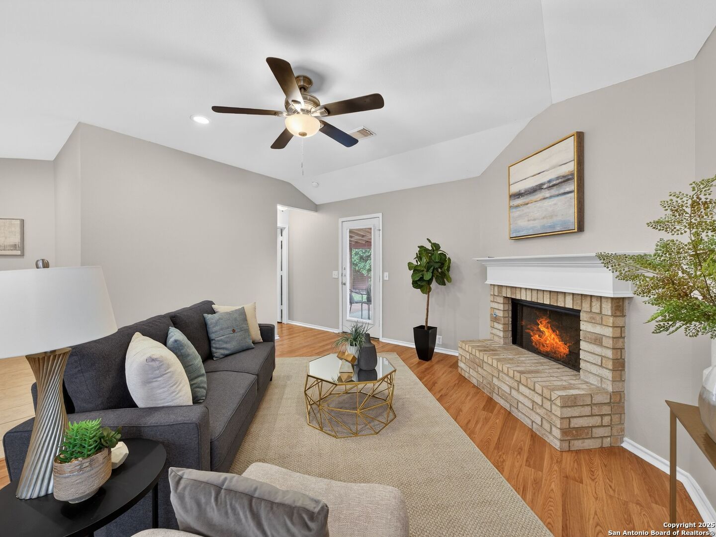 Living room with a brick fireplace, vaulted ceiling, ceiling fan, and gray seating.