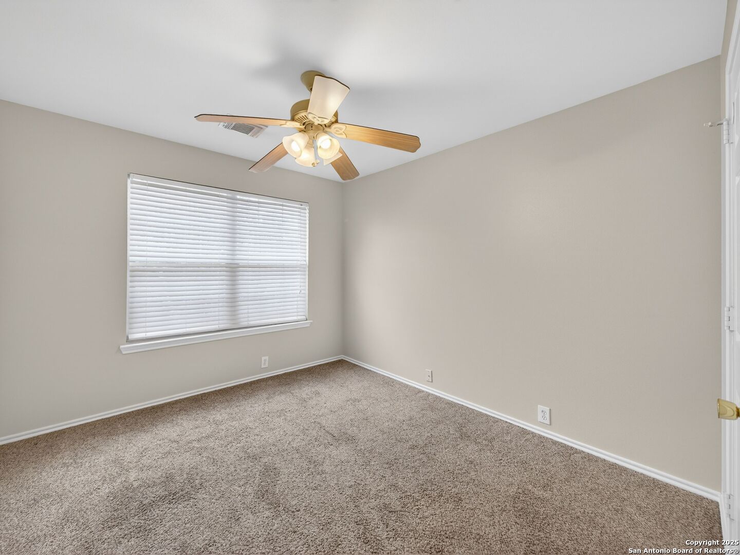 Empty bedroom with beige carpet, a ceiling fan, and a wide window with white blinds.