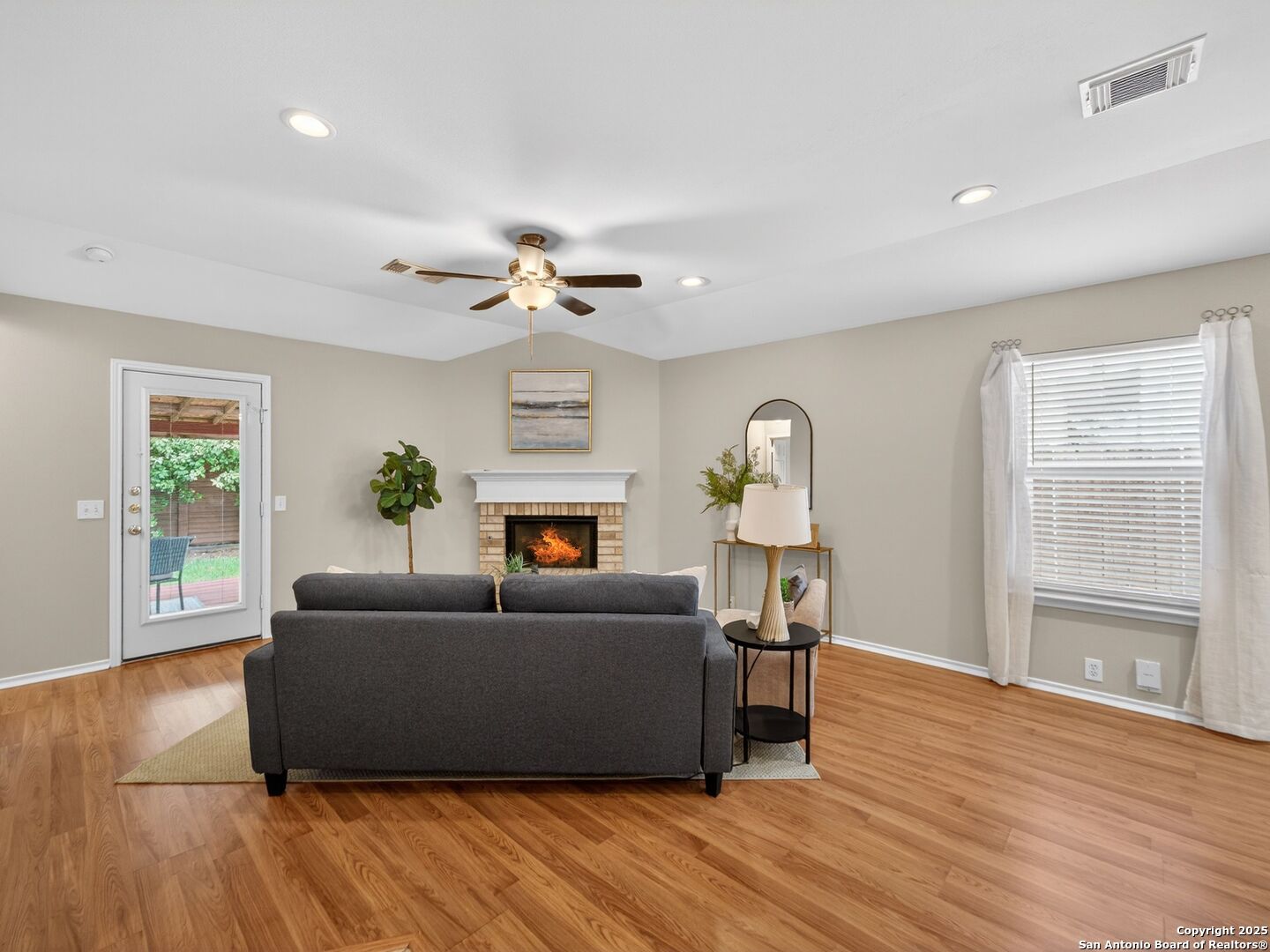 Staged living room with a brick fireplace, gray sofa, hardwood floors, and glass patio door.