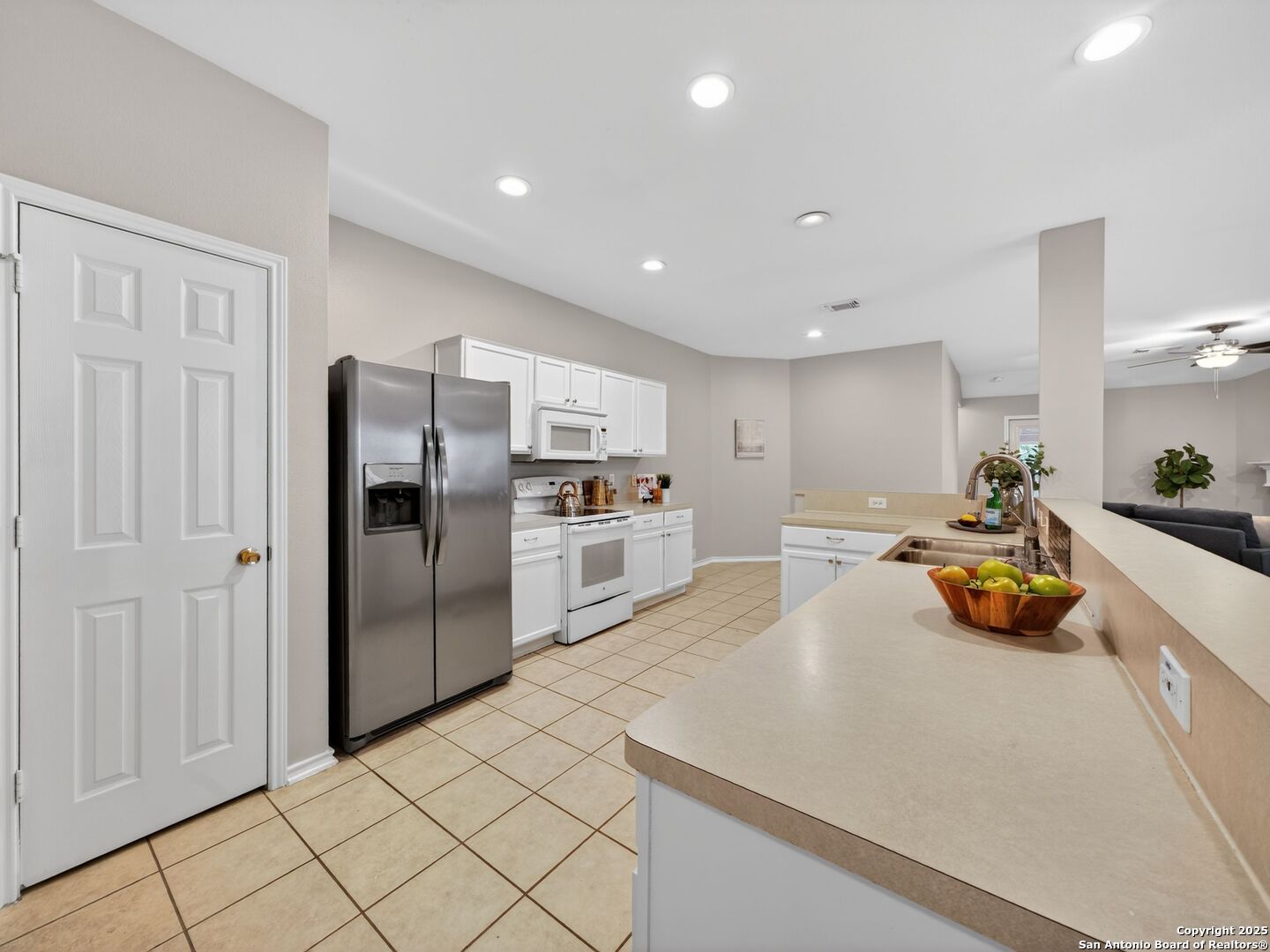 Open kitchen with white cabinets, stainless steel appliances, and a long peninsula with a double sink.