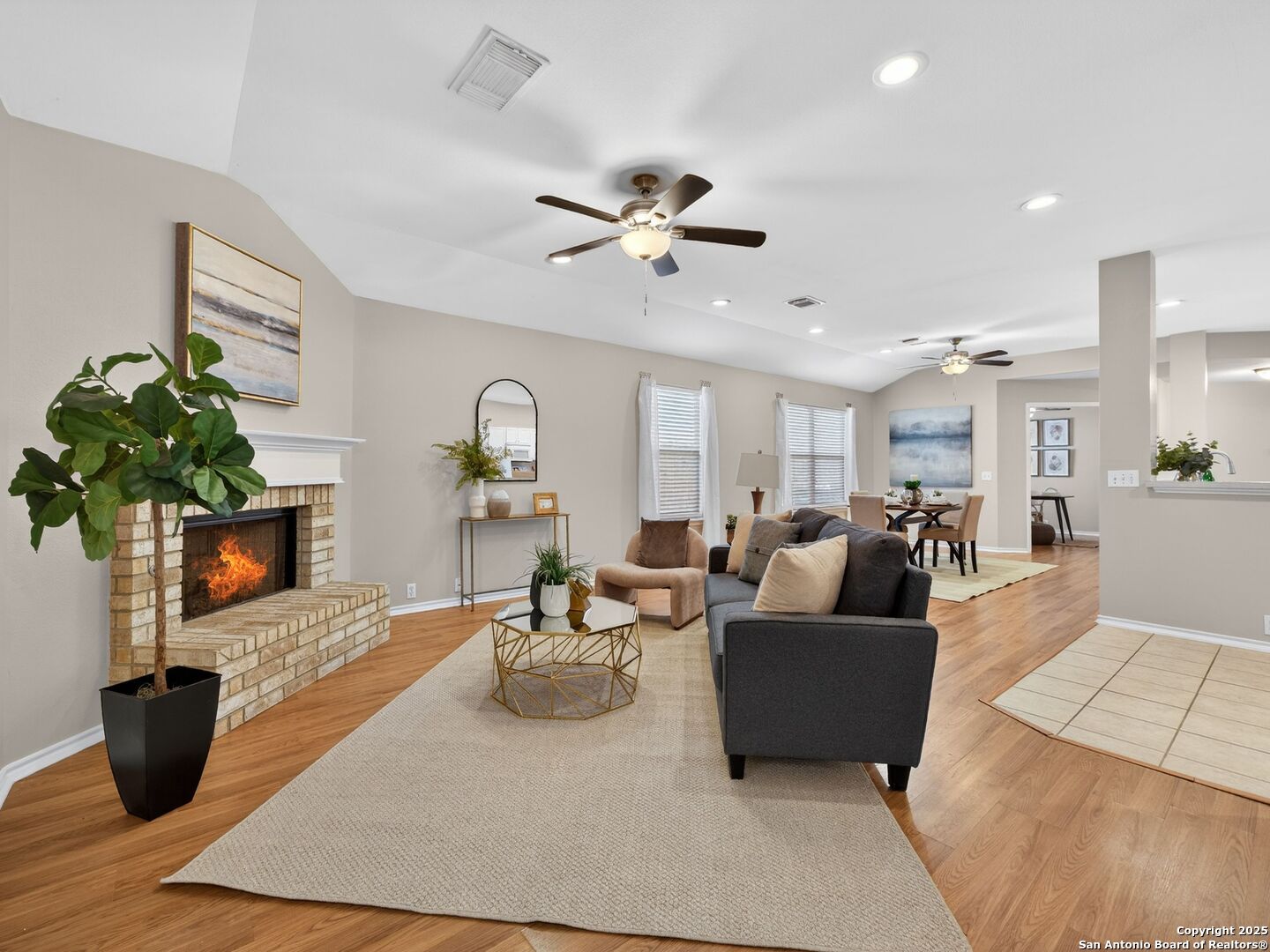 Open living and dining area with a brick fireplace, ceiling fans, and neutral furnishings.