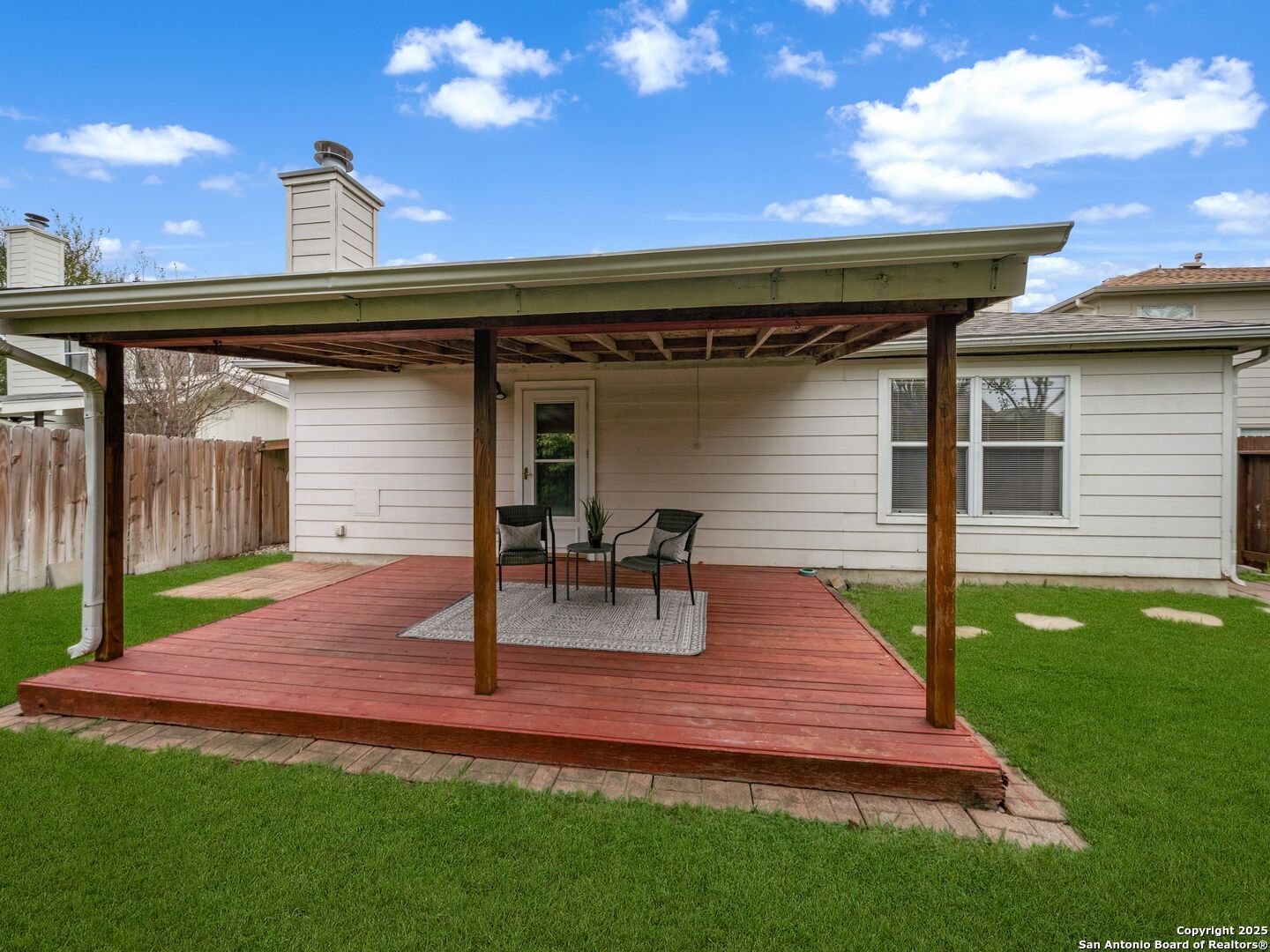 Covered red-wood deck with seating behind a house, overlooking a green lawn.