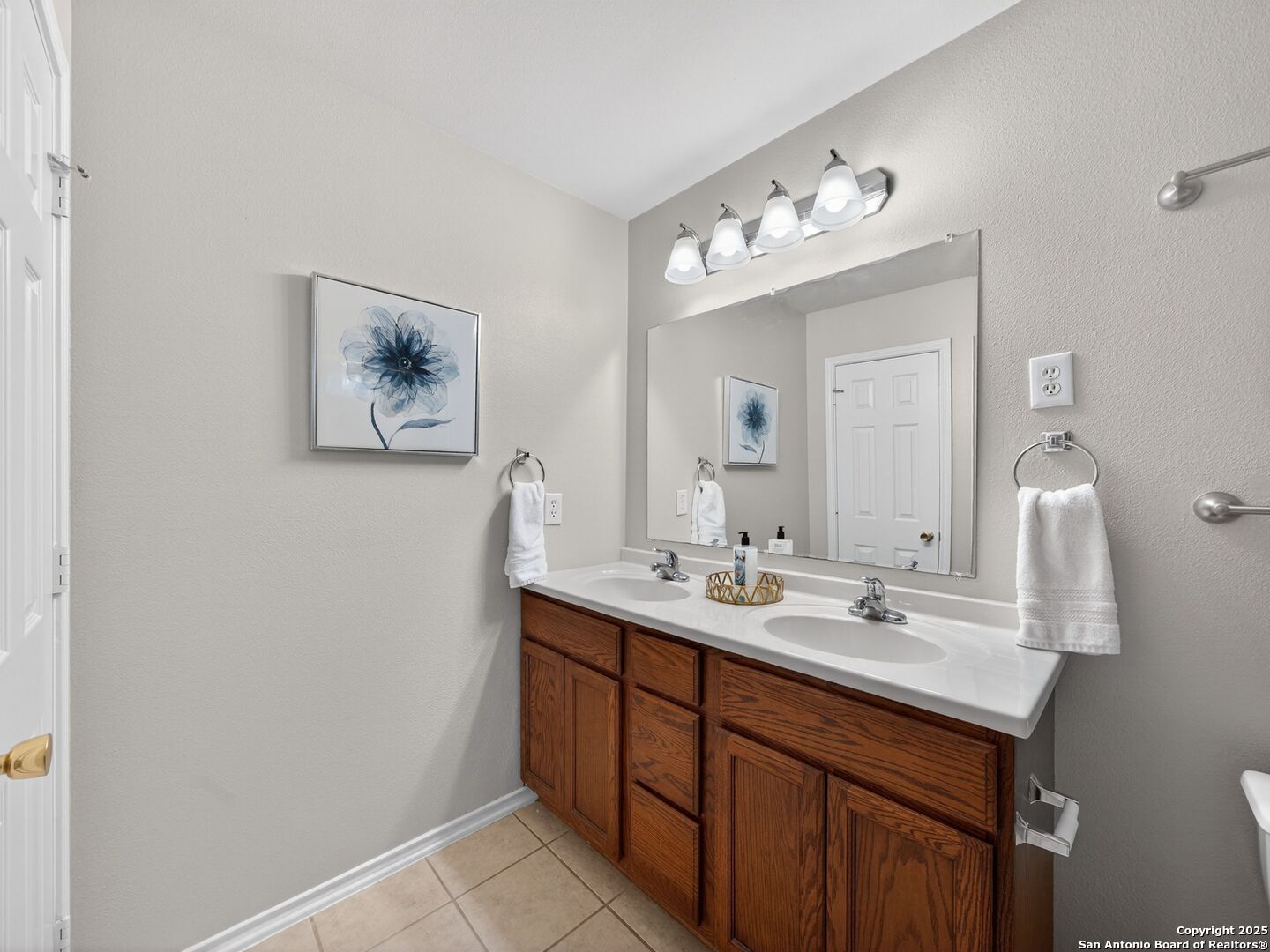 Bathroom with a double-sink vanity, reddish-brown wood cabinets, and a large wall mirror.