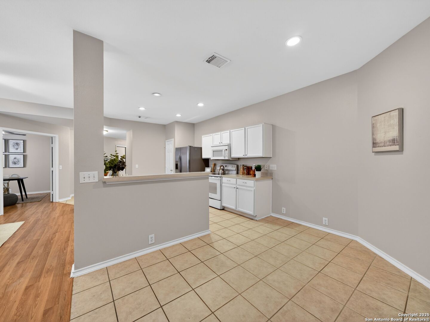 Kitchen and dining area with white cabinets, a breakfast bar, and tan tile flooring.