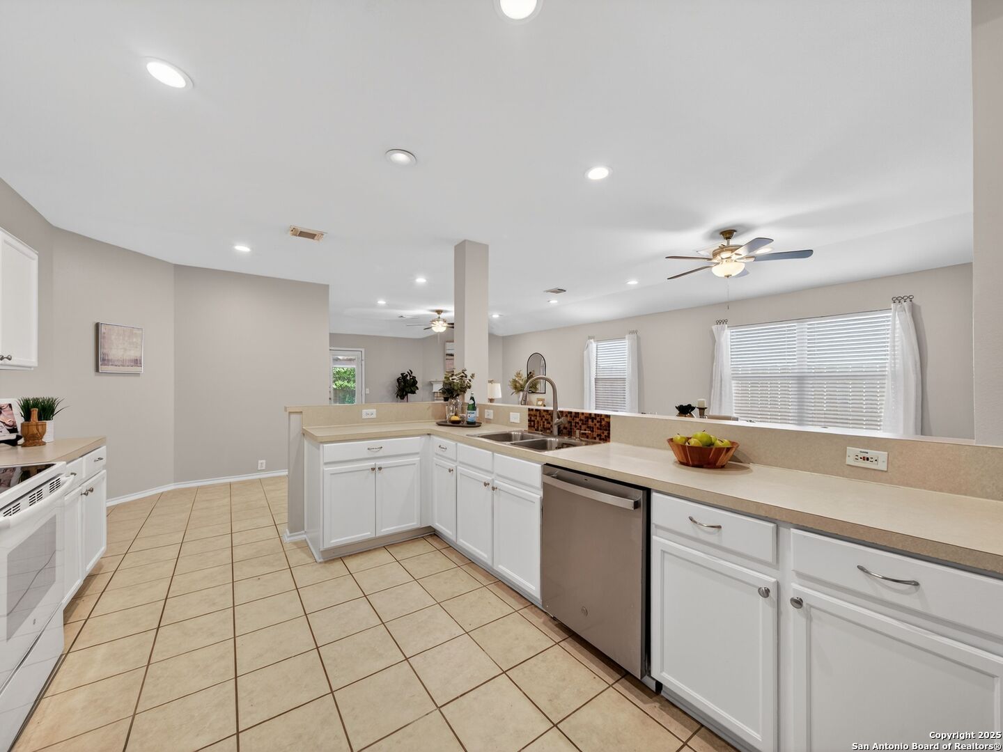 Kitchen with white cabinetry, beige counters, stainless-steel dishwasher, and tan tile flooring.