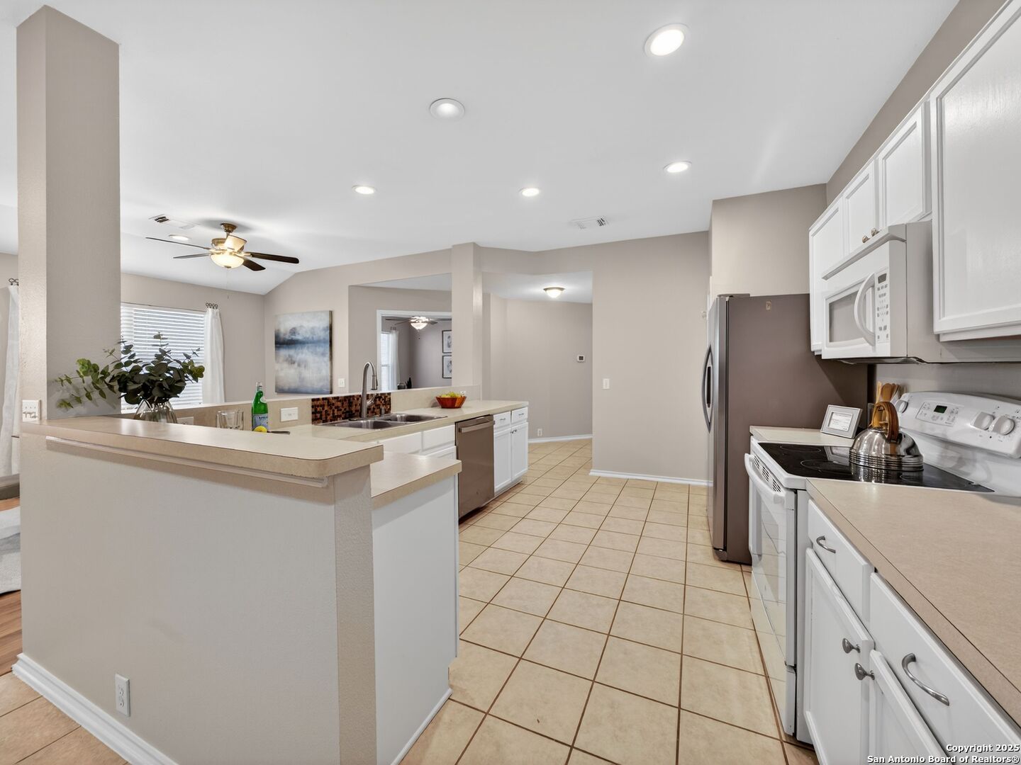 Kitchen with a long breakfast peninsula, white cabinetry, stainless steel appliances, and beige tile flooring.