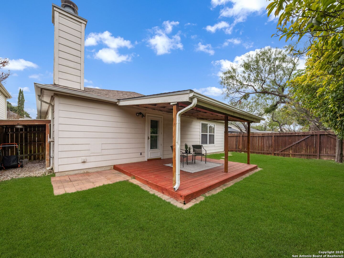 Home’s rear exterior with a covered redwood deck, patio seating, and fenced green backyard.
