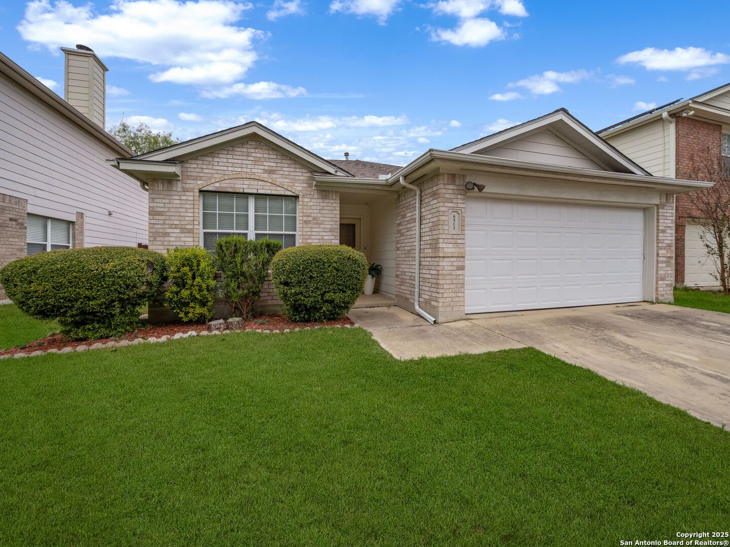 Single-story brick house with a two-car garage, covered entry, and neatly trimmed front lawn.