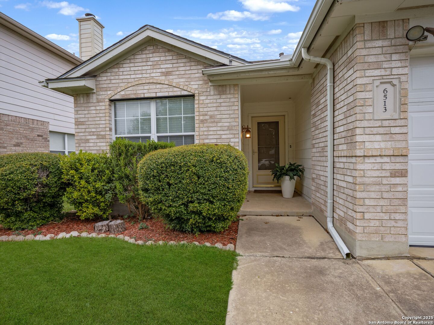 Light brick house with a covered entry, trimmed hedges, and a concrete walkway to the front door.